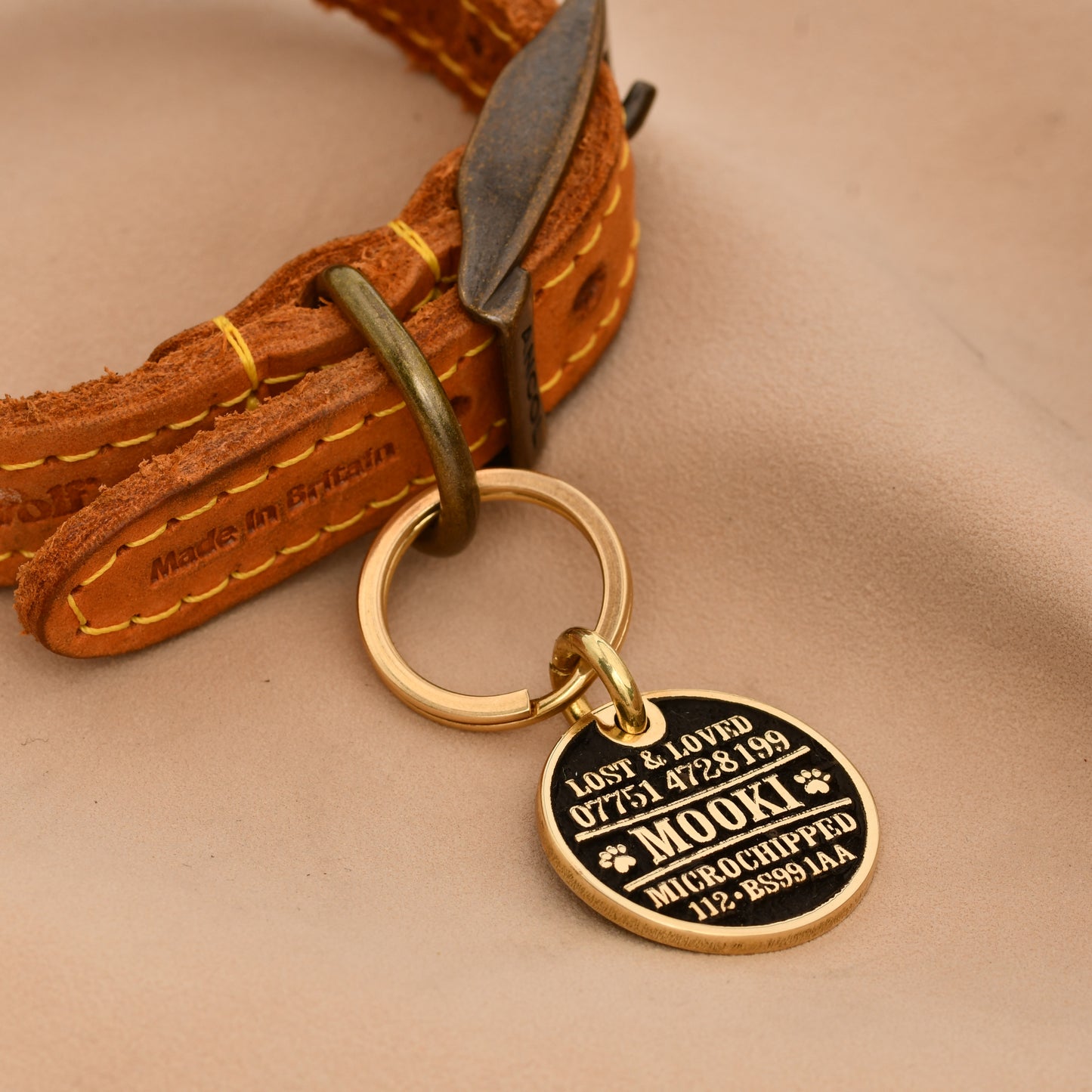 Brass round dog ID tag with deep engraving, handmade in the UK, shown on a collar for size reference.