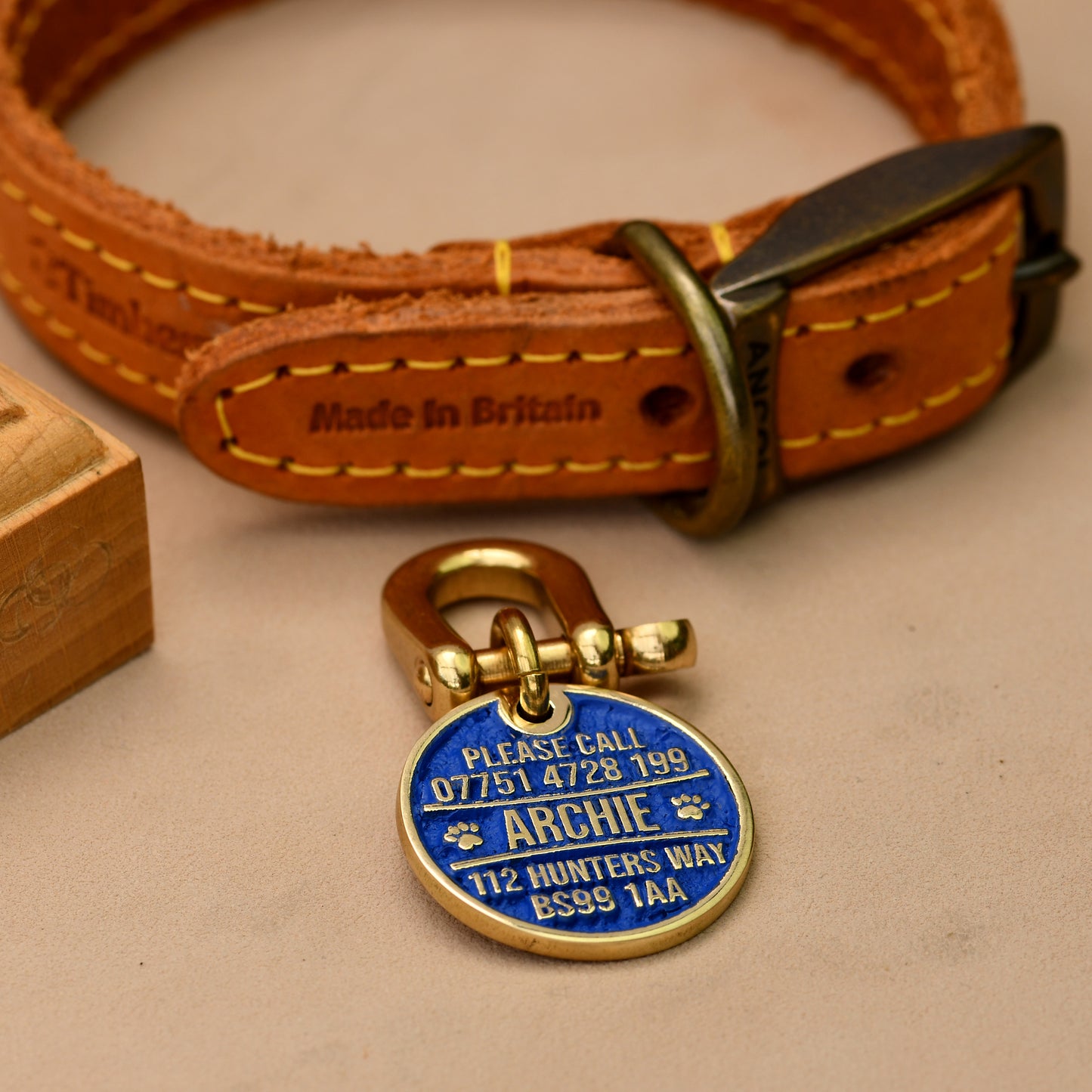 Brass round dog ID tag with deep engraving, handmade in the UK, shown on a collar for size reference.