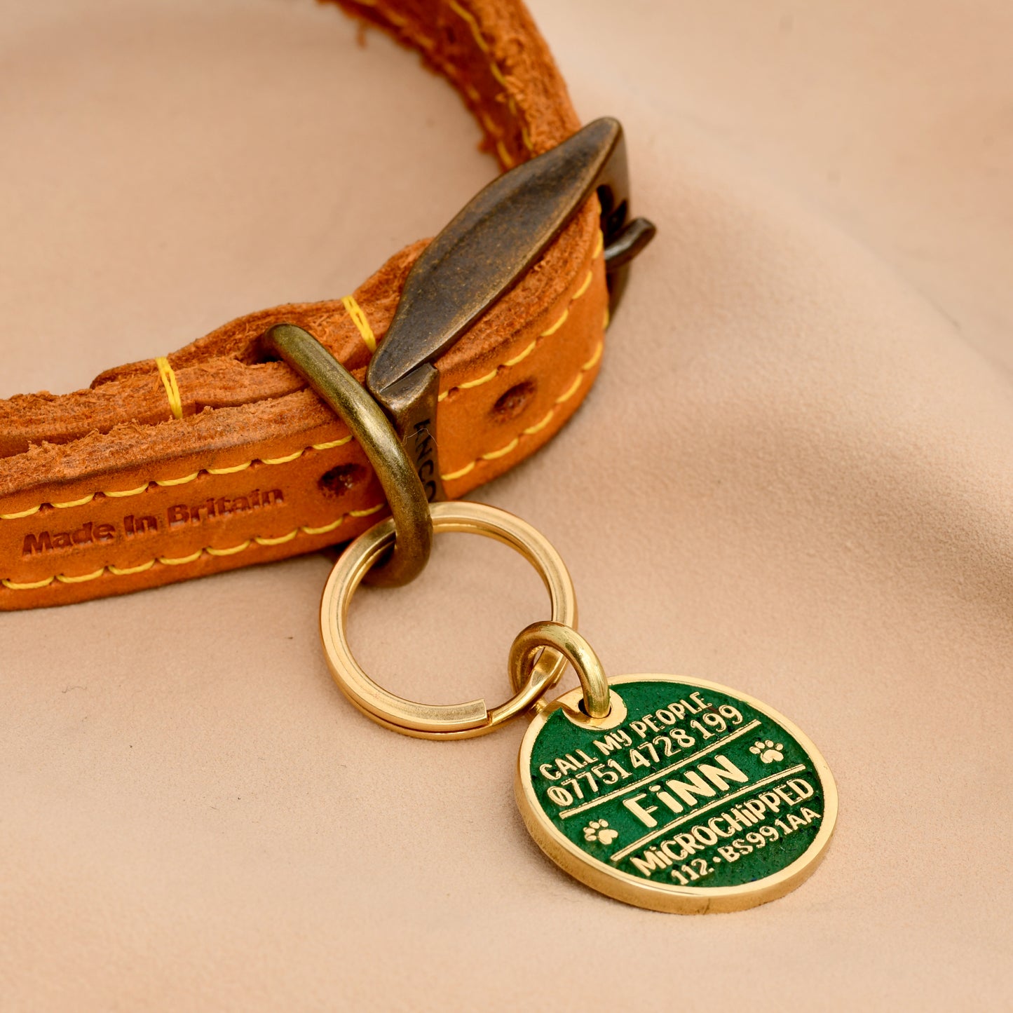 Brass round dog ID tag with deep engraving, handmade in the UK, shown on a collar for size reference.