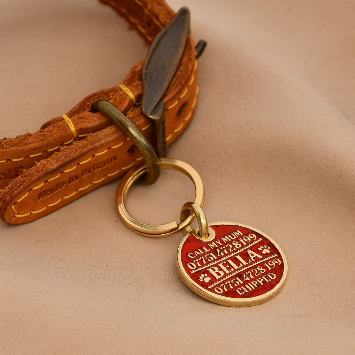 Brass round dog ID tag with deep engraving, handmade in the UK, shown on a collar for size reference.