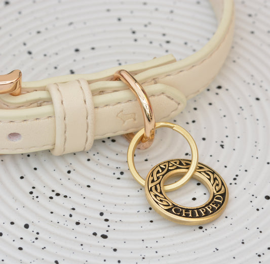 Hoop-shaped brass ID tag with engraved Celtic pattern, handmade in the UK. Suitable for dogs, cats, and horse bridles. Shown attached to a collar for display.