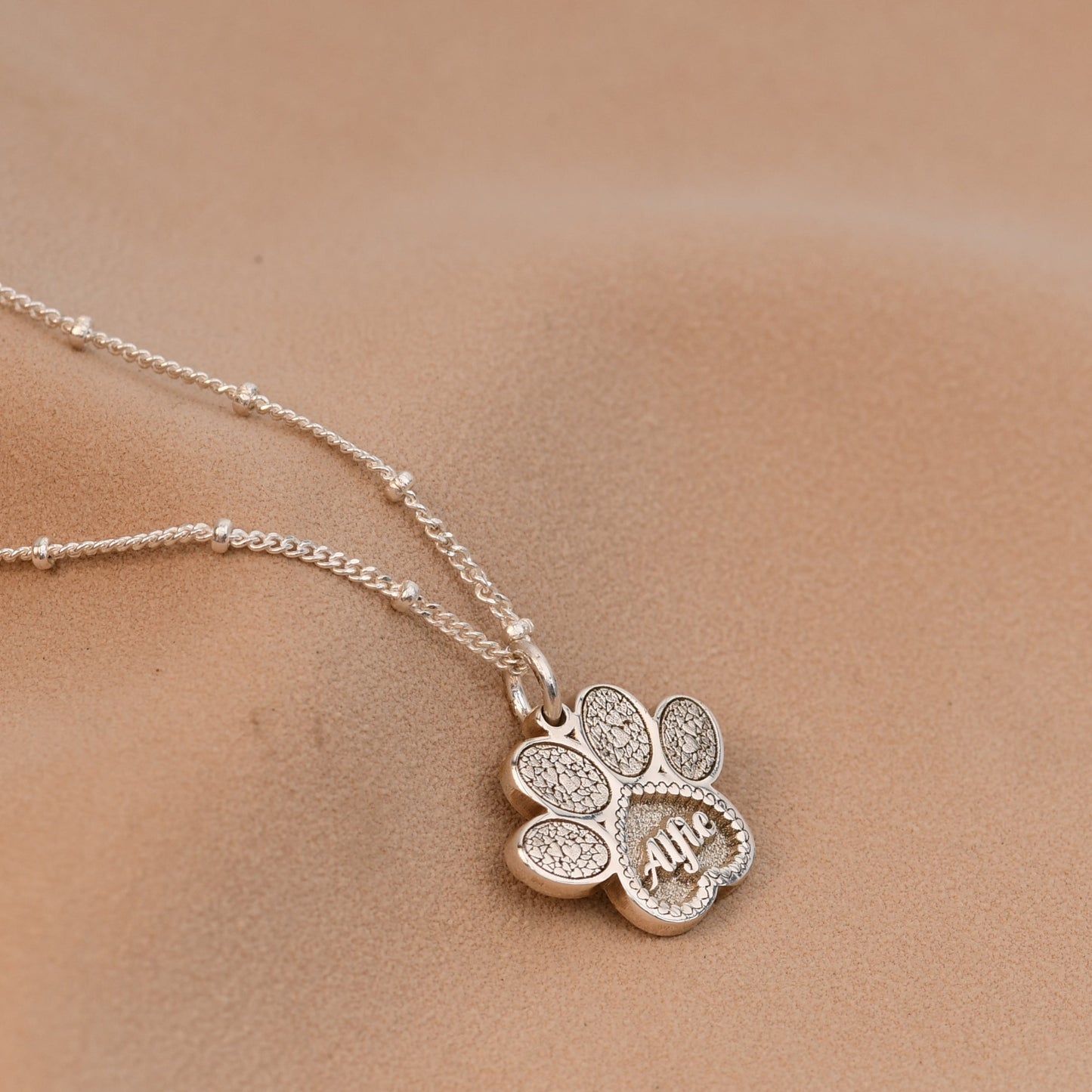 Silver necklace with a clover pendant on a person's neck against a neutral background