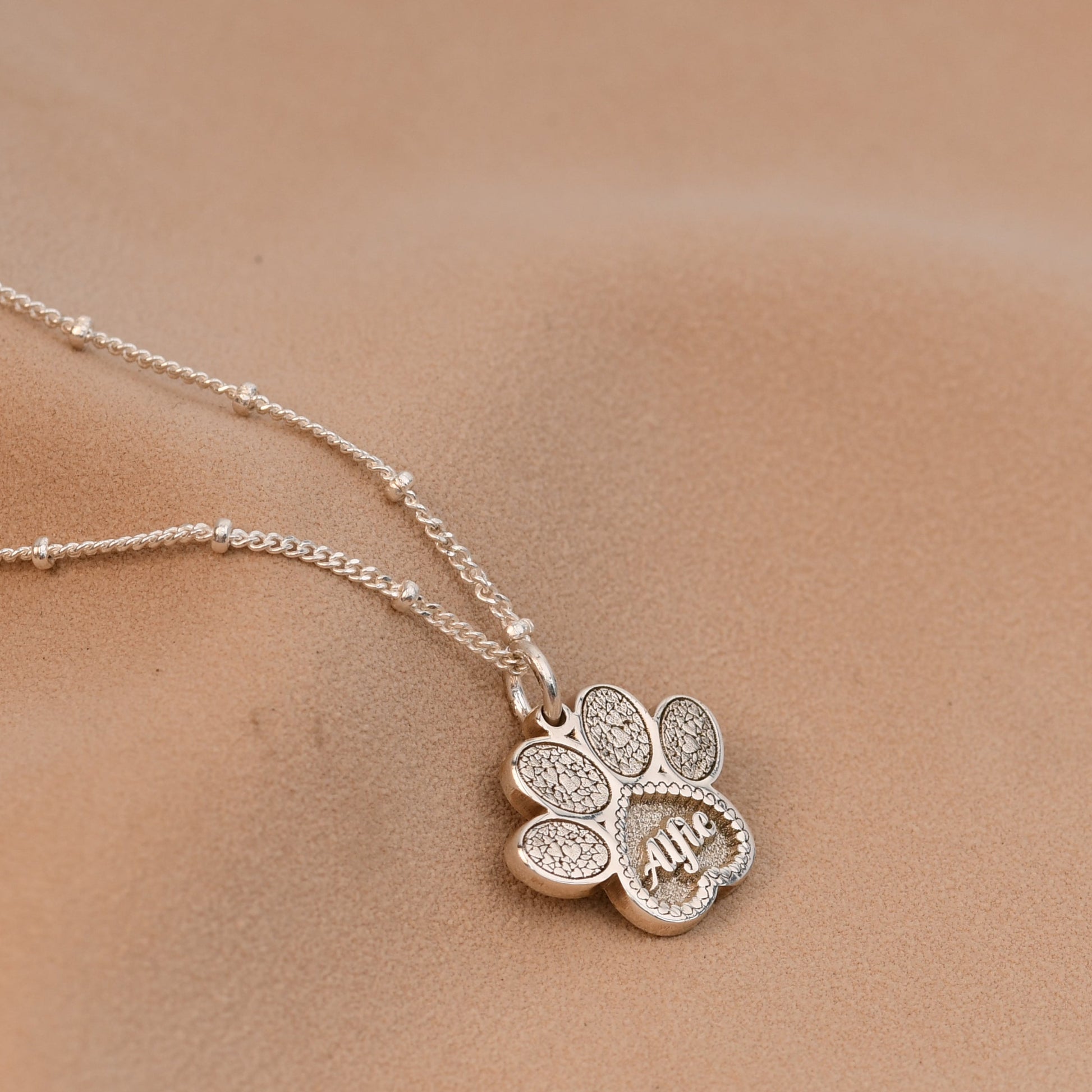 Silver necklace with a clover pendant on a person's neck against a neutral background