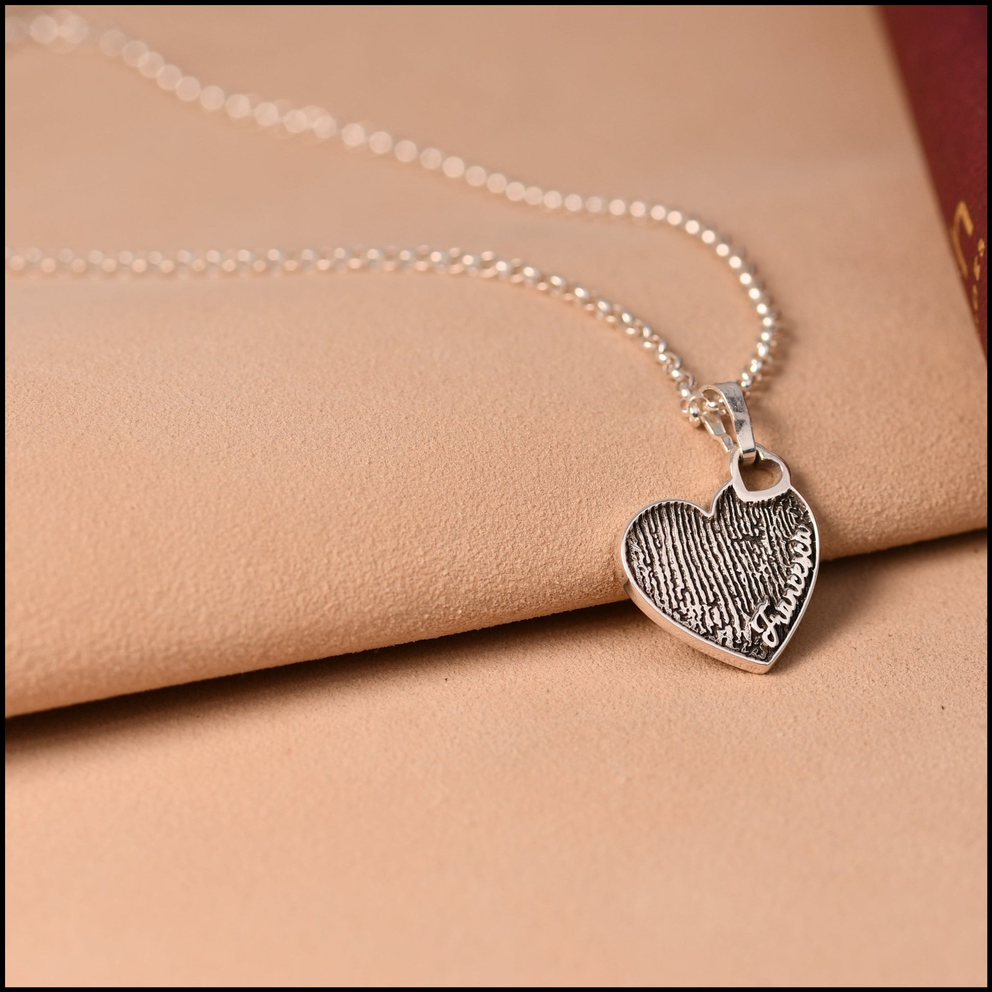Silver necklace with a heart-shaped pendant on a beige fabric background