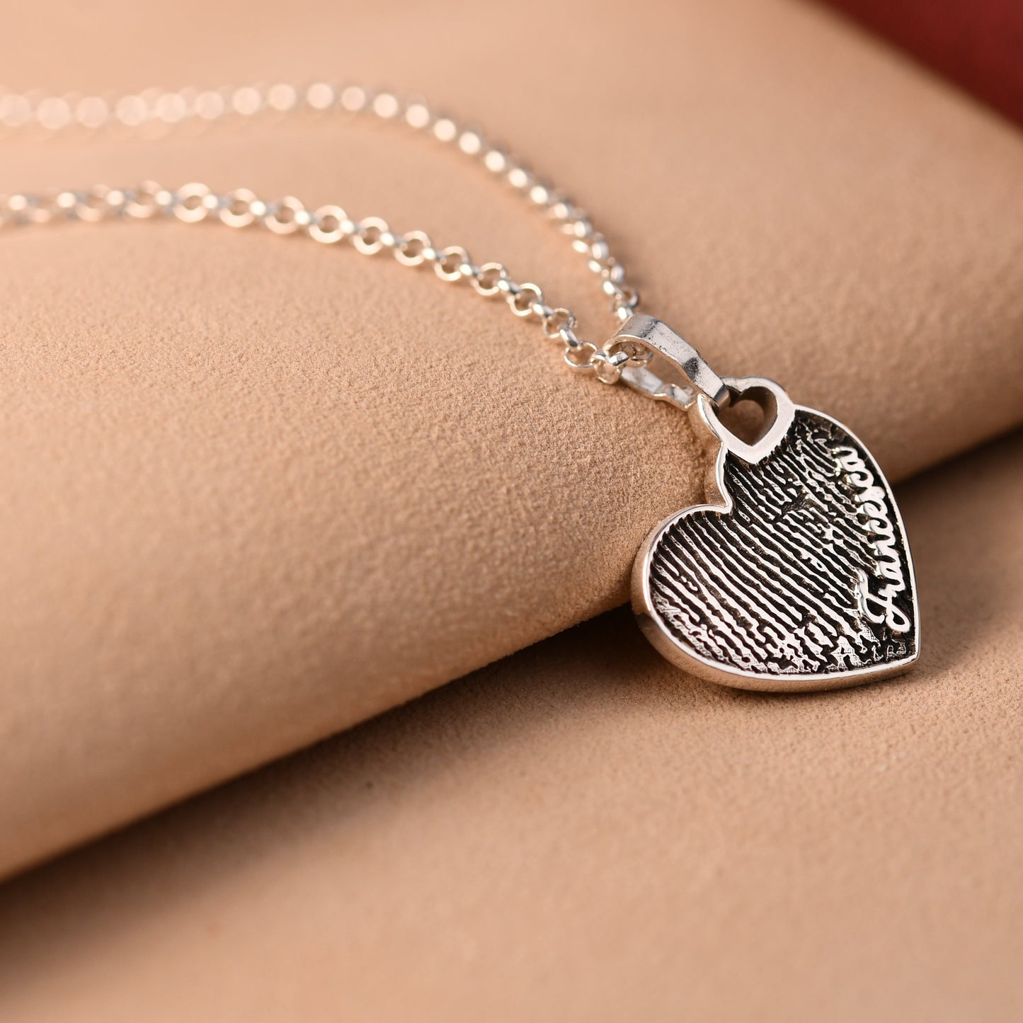 Silver heart-shaped necklace with engraved design on a beige surface.