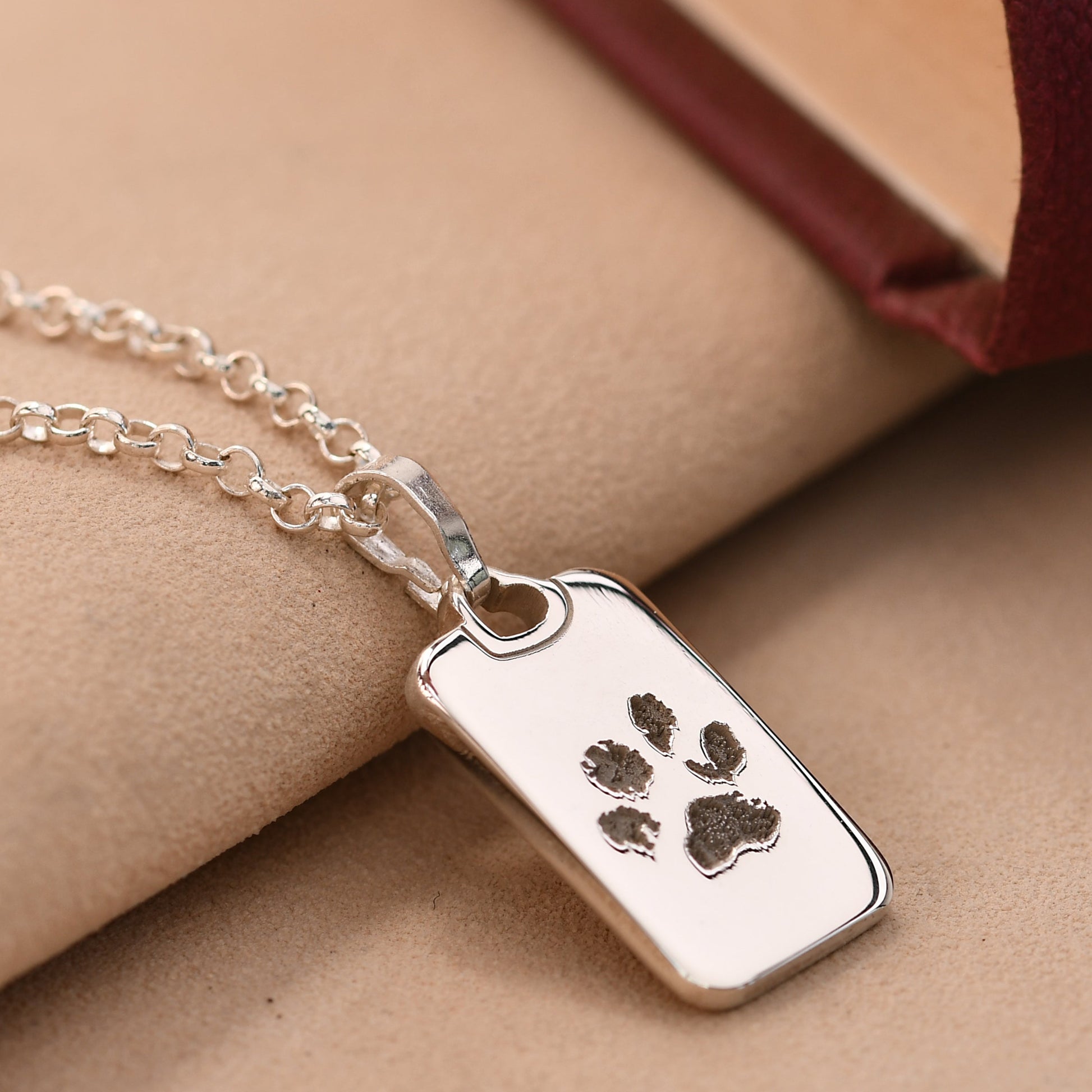 Silver necklace with a paw print pendant on a beige surface.
