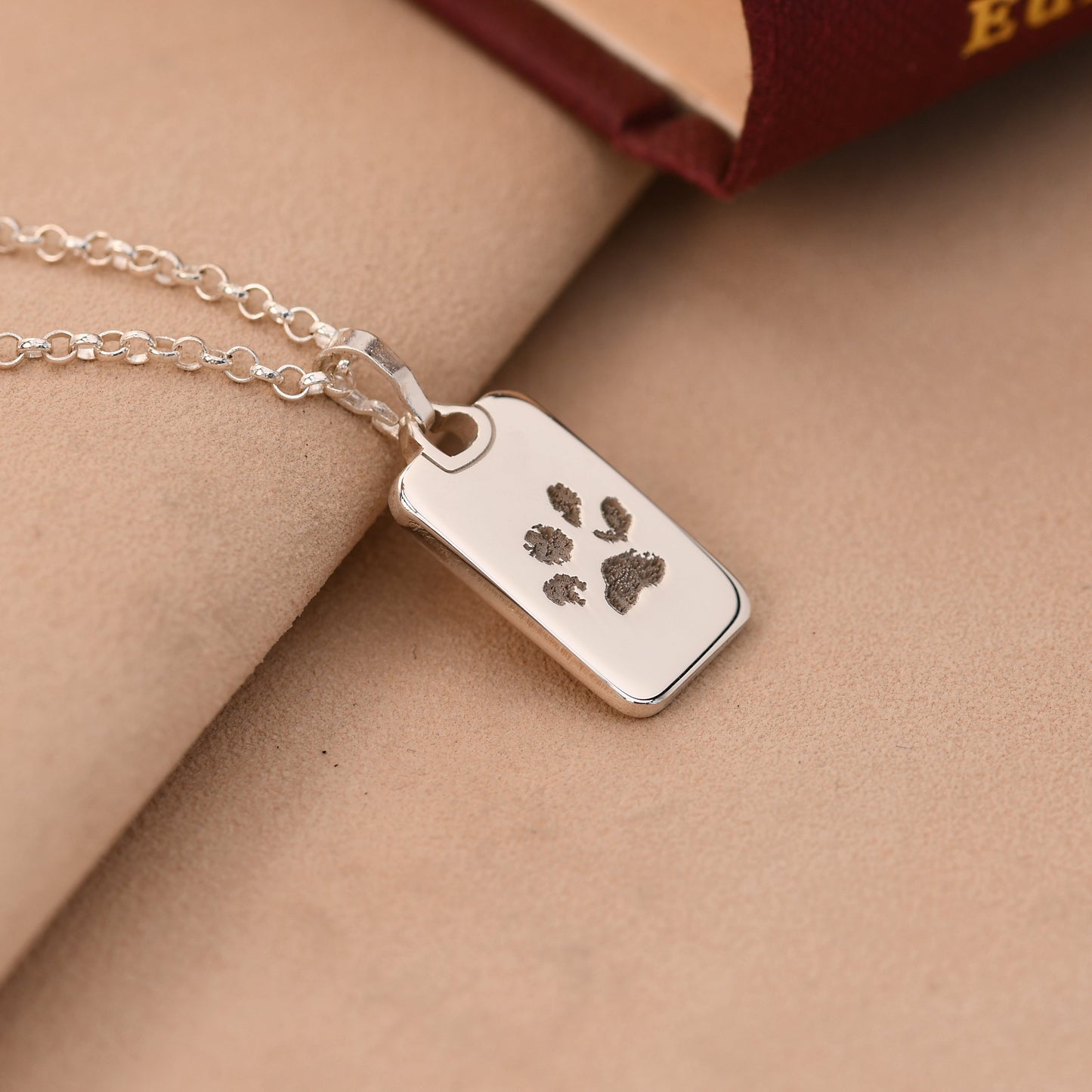 Silver necklace with a paw print tag on a beige surface