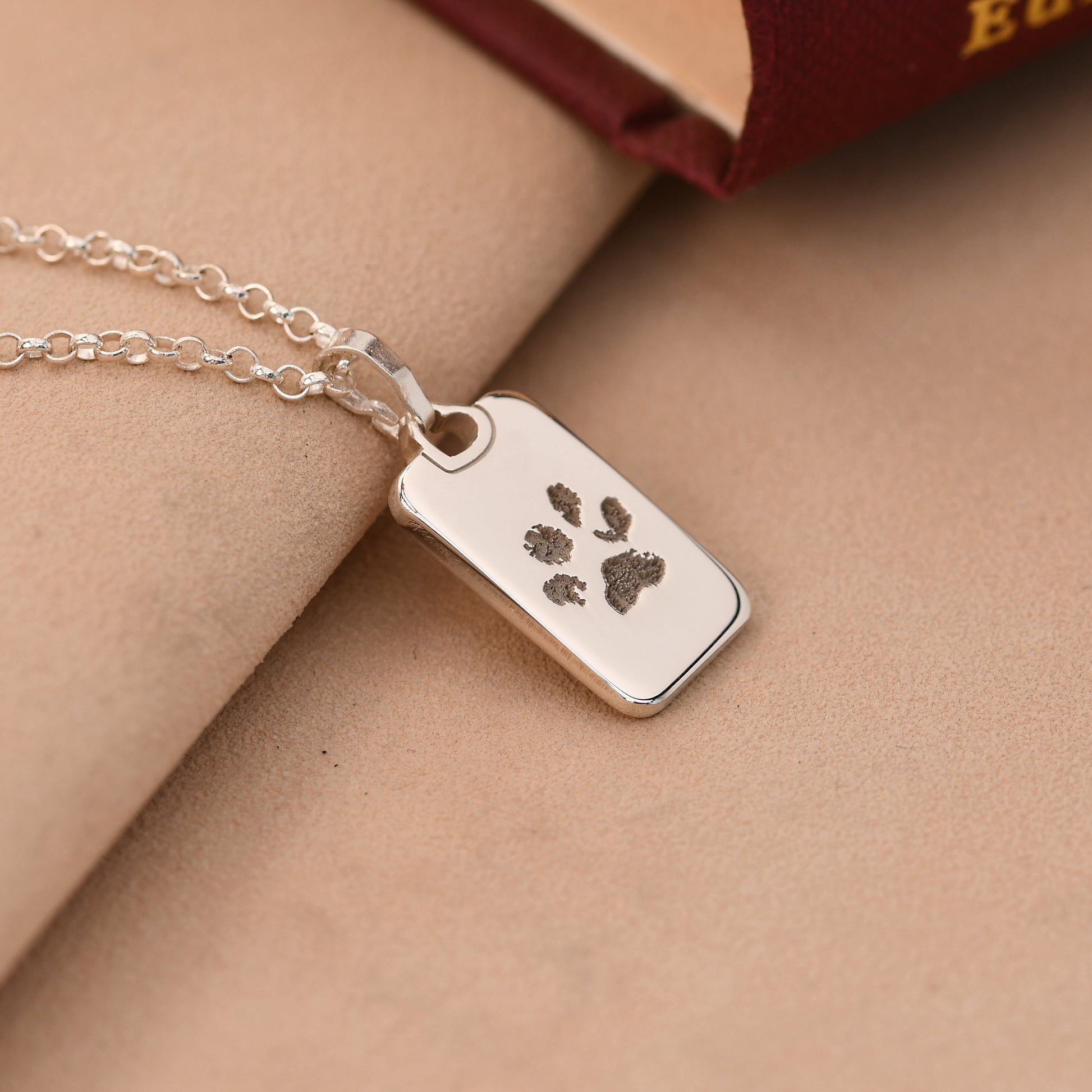 Silver necklace with a paw print tag on a beige surface