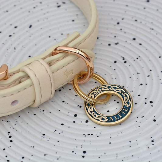 Hoop-shaped brass ID tag with engraved Celtic pattern, handmade in the UK. Suitable for dogs, cats, and horse bridles. Shown attached to a collar for display.