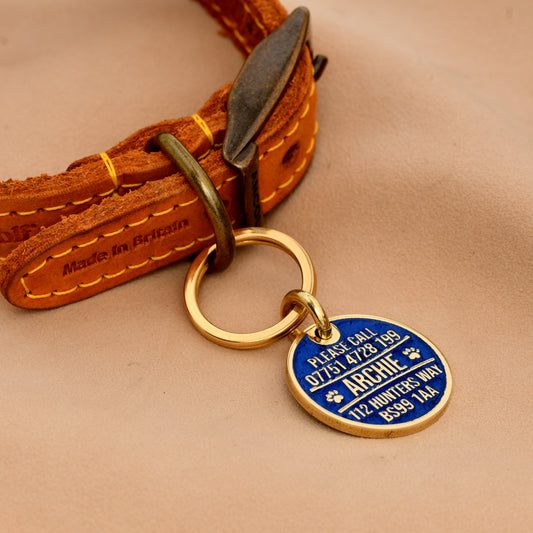Brass round dog ID tag with deep engraving, handmade in the UK, shown on a collar for size reference.