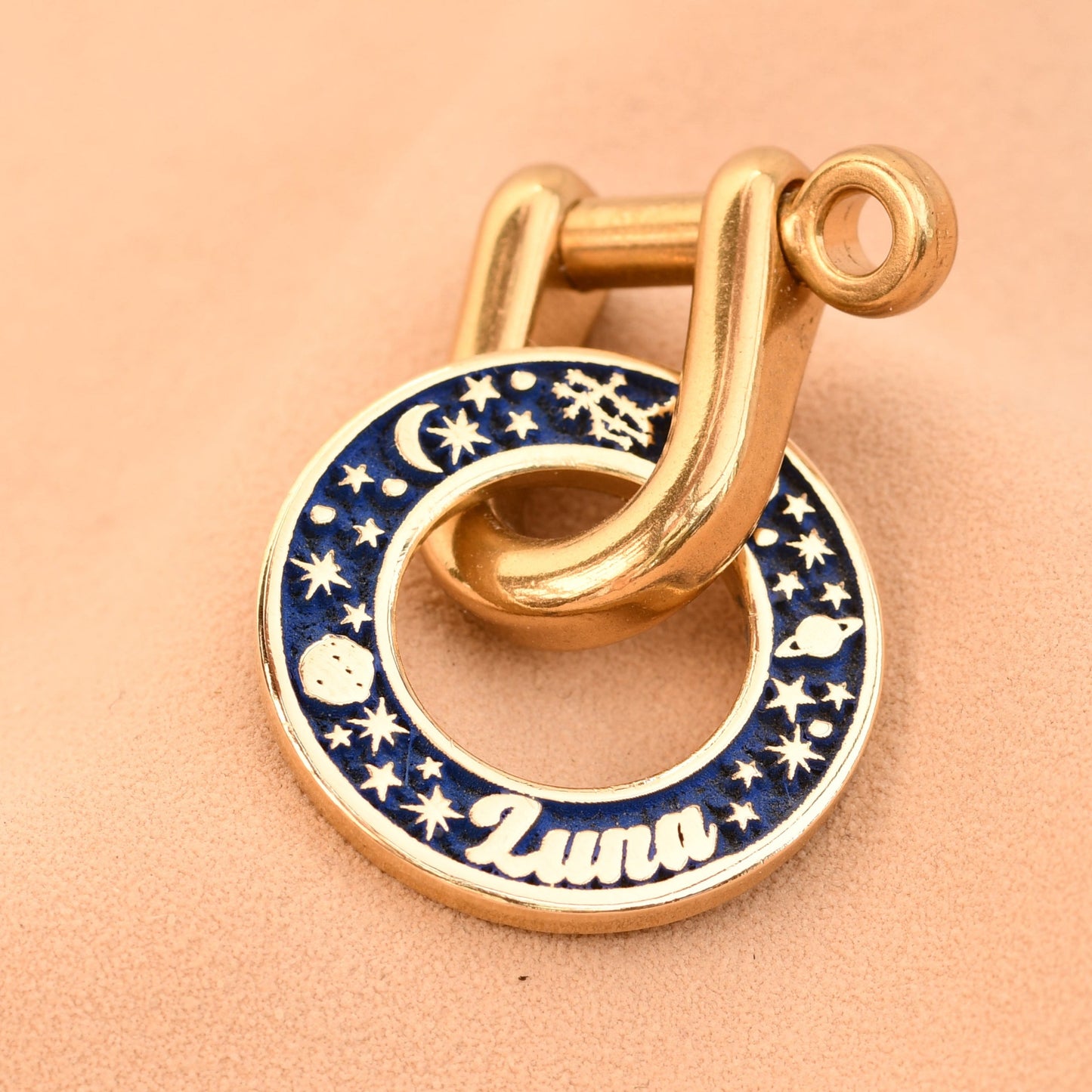 Gold charm with blue enameled design on a beige background