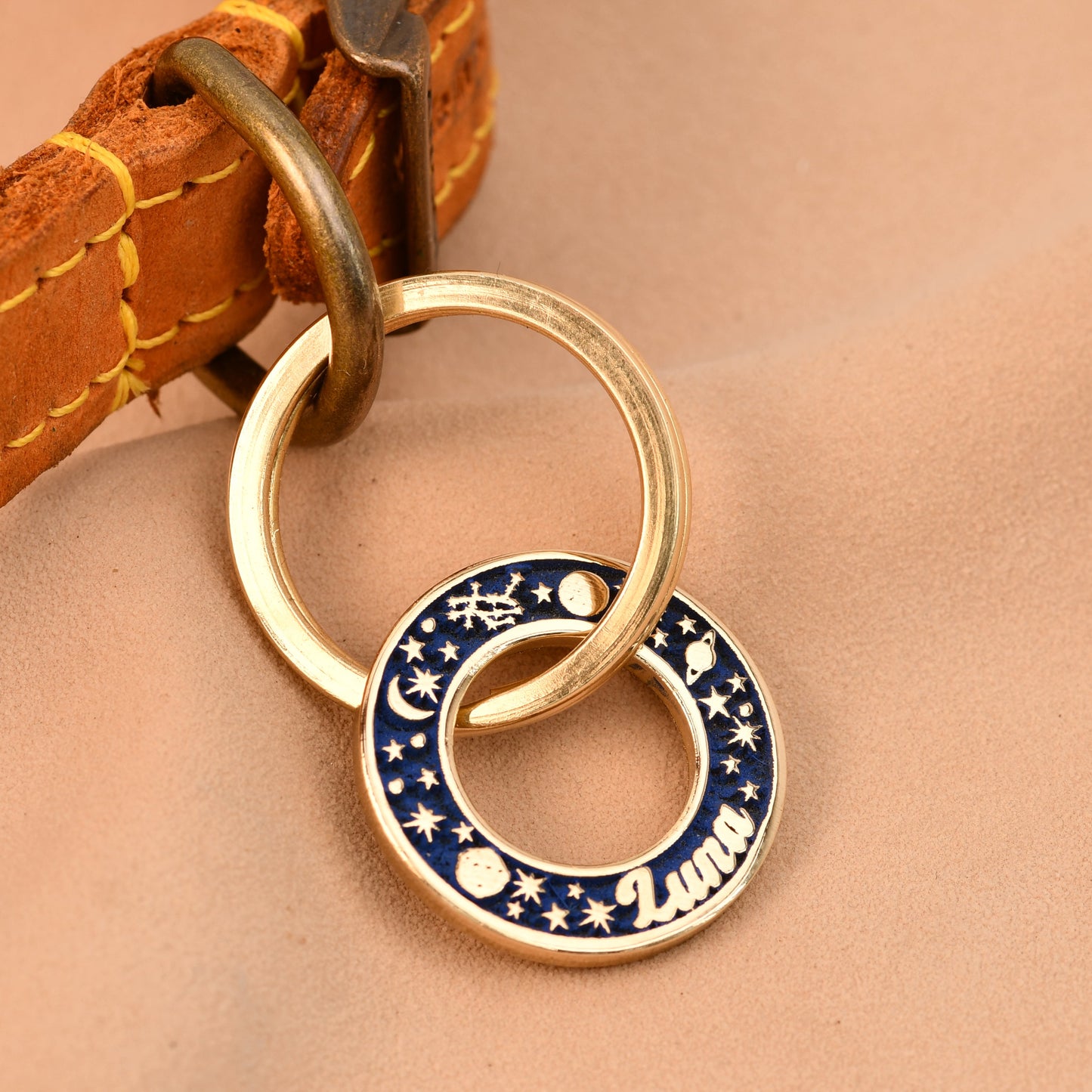 Dog collar with a gold ring and blue engraved tag on a beige background
