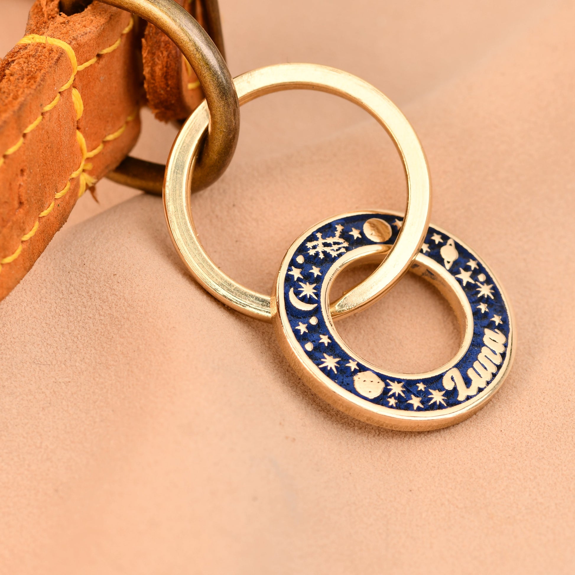 Gold and blue circular keychain on a leather strap against a beige background
