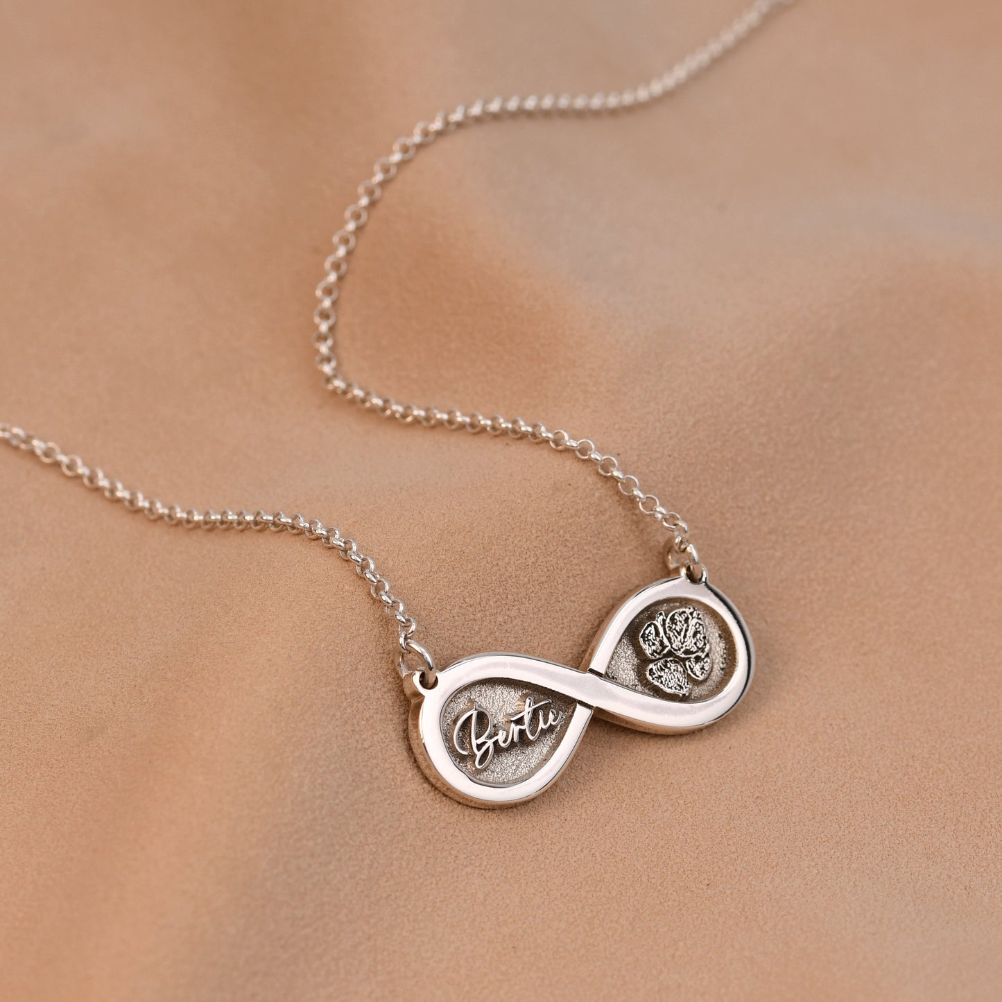 Silver infinity necklace with engraved names on a beige background