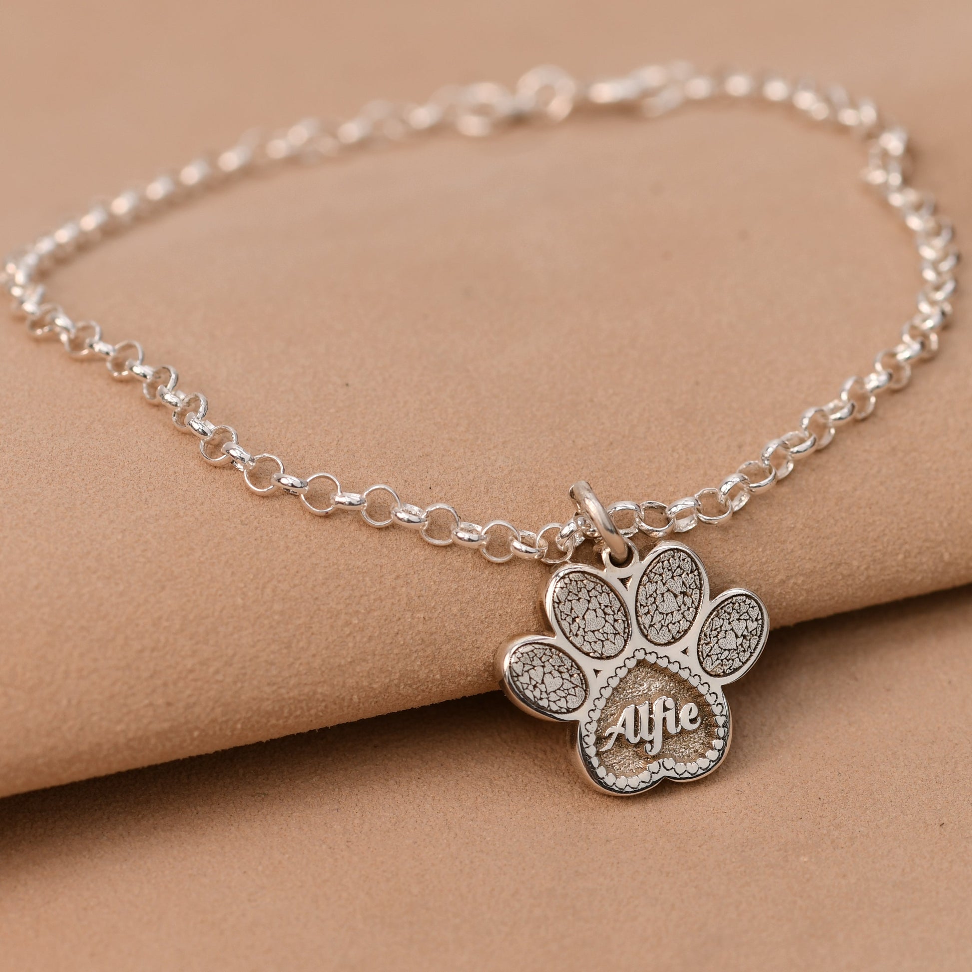 Silver bracelet with a paw charm on a beige surface