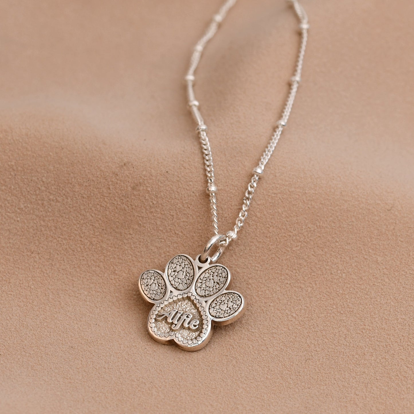 Silver necklace with a paw-shaped pendant on a beige fabric background