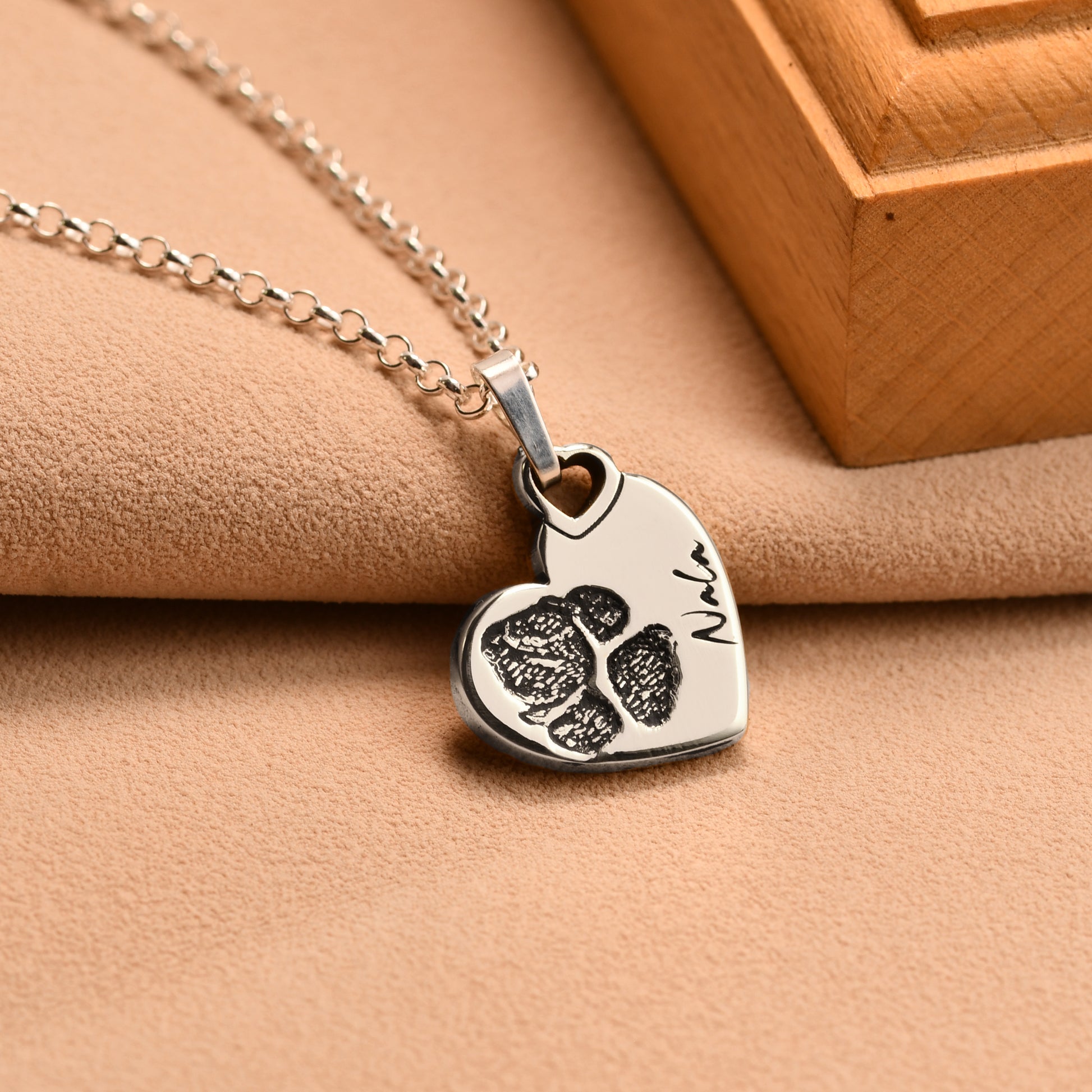 Heart-shaped pendant with paw print and name on a beige surface