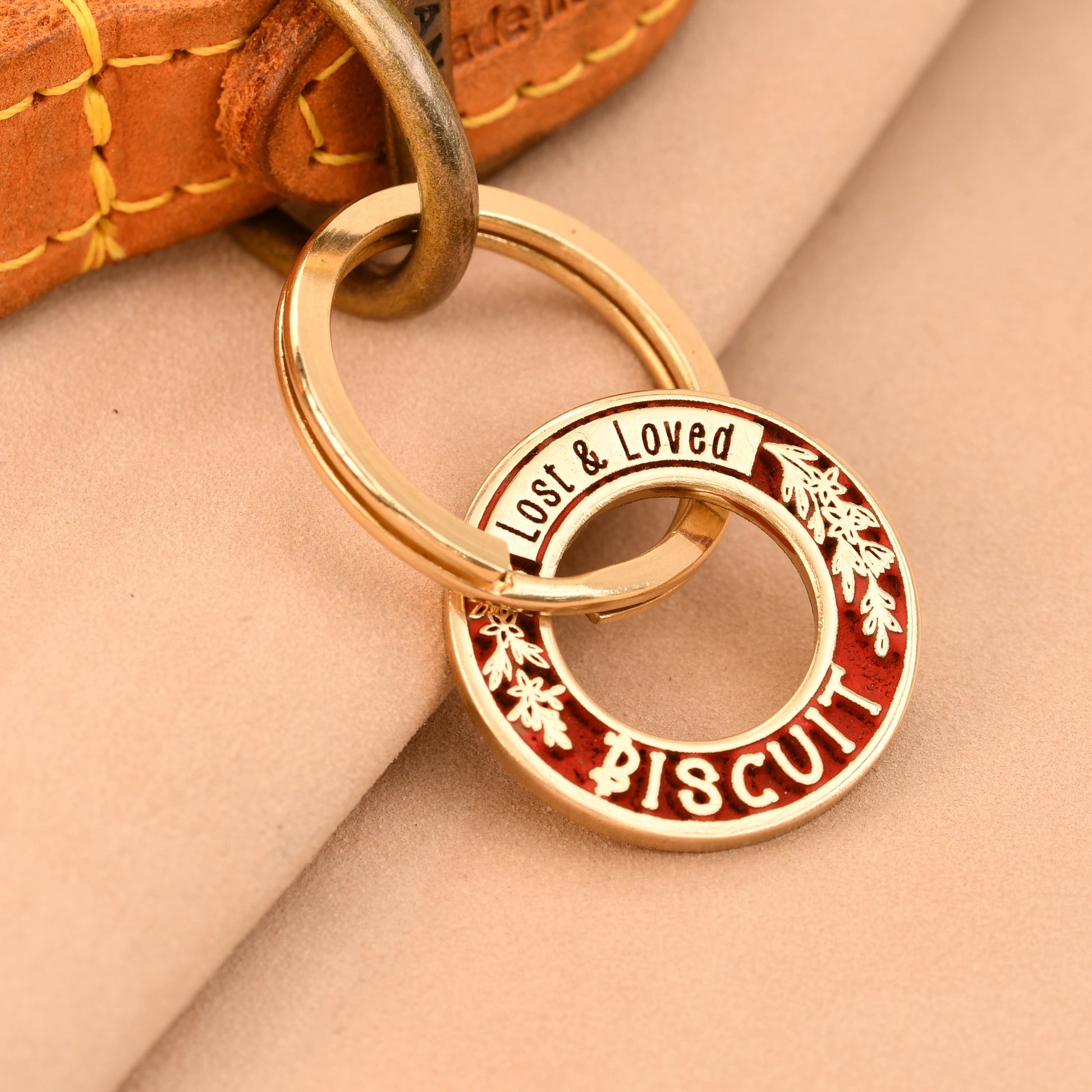Gold dog tag with 'Loved & Loved' branding on a beige background