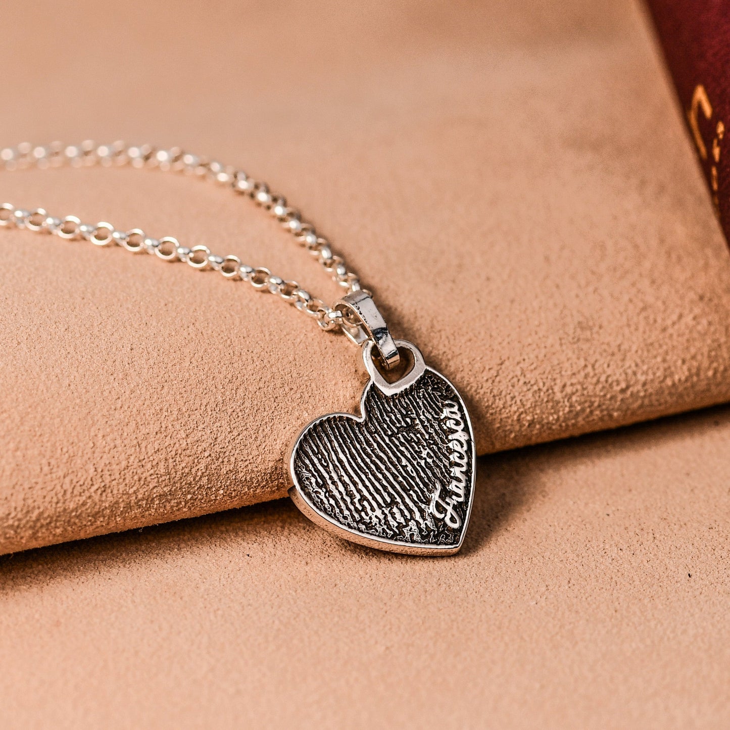 Silver necklace with a heart-shaped pendant on a leather surface with an open book.