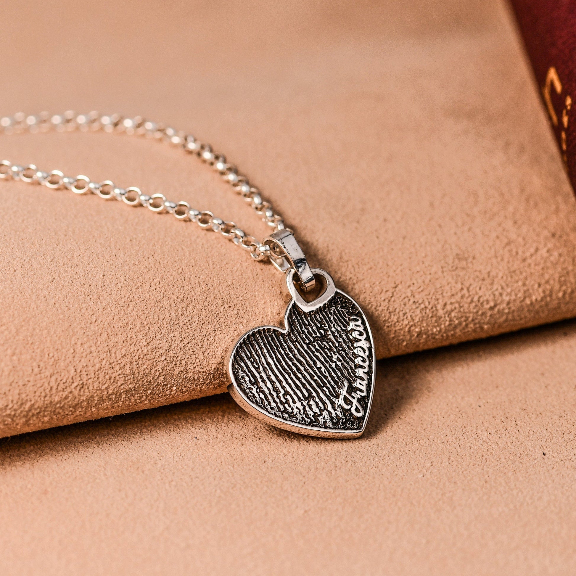 Silver necklace with a heart-shaped pendant on a leather surface with an open book.