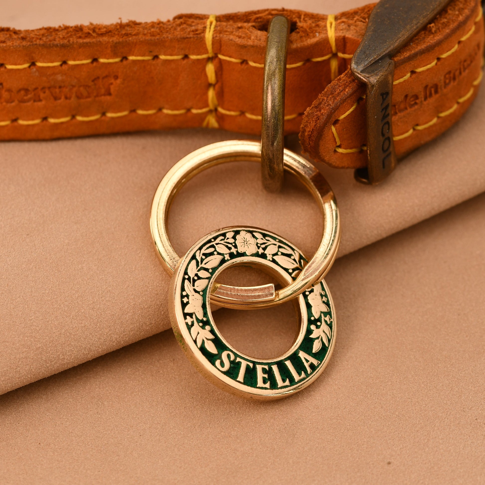Gold dog collar with a engraved tag on a beige fabric background