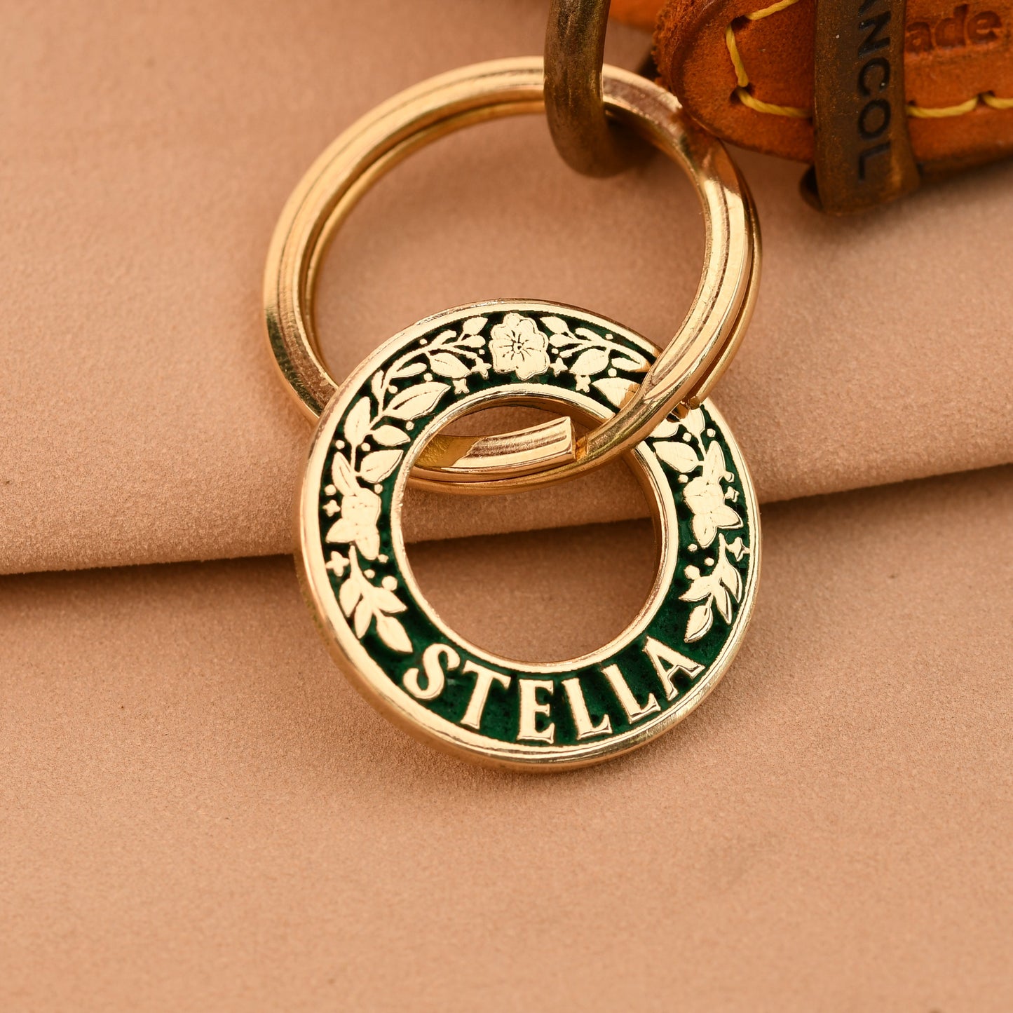 Gold and green keychain with 'Stella' branding on a beige surface