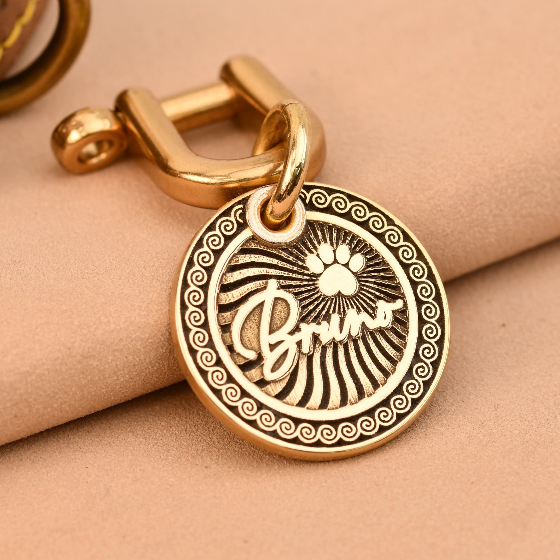 Gold dog tag with paw print design on a beige surface