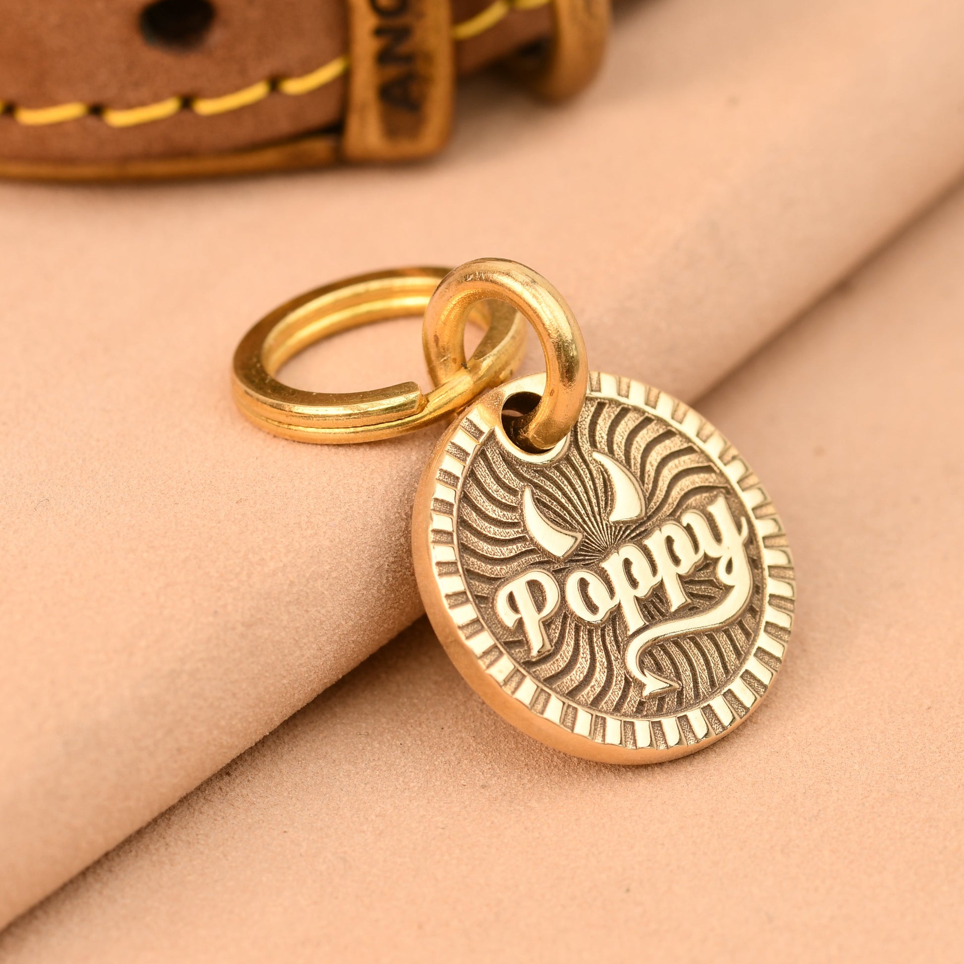 Gold dog tag with 'Poppy' engraved on a beige fabric background