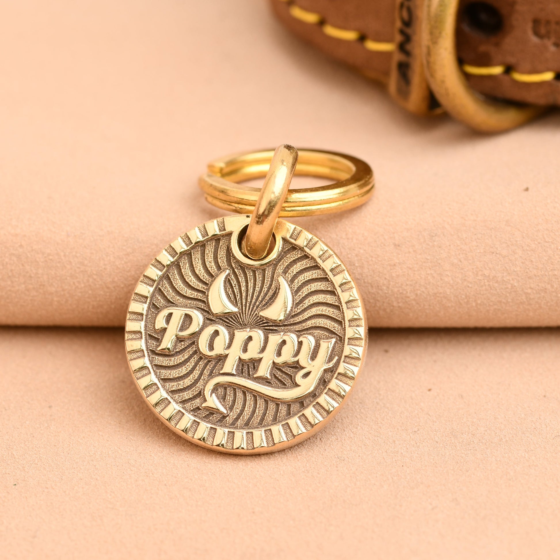 Gold pendant with 'Poppy' engraved on a beige fabric background