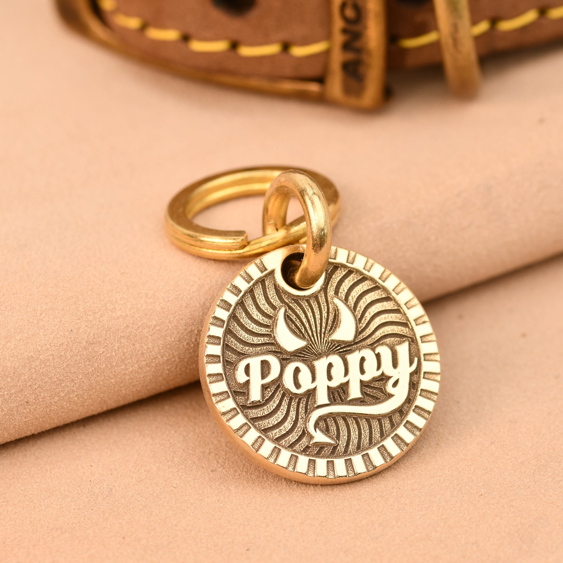 Gold pendant with 'Poppy' engraved on a beige fabric background