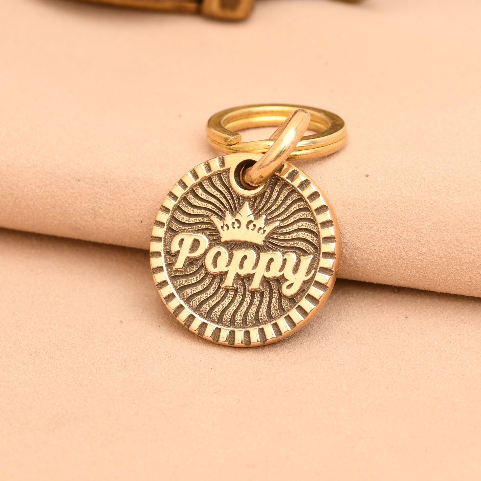 Gold dog tag with 'Poppy' engraved on a beige fabric background