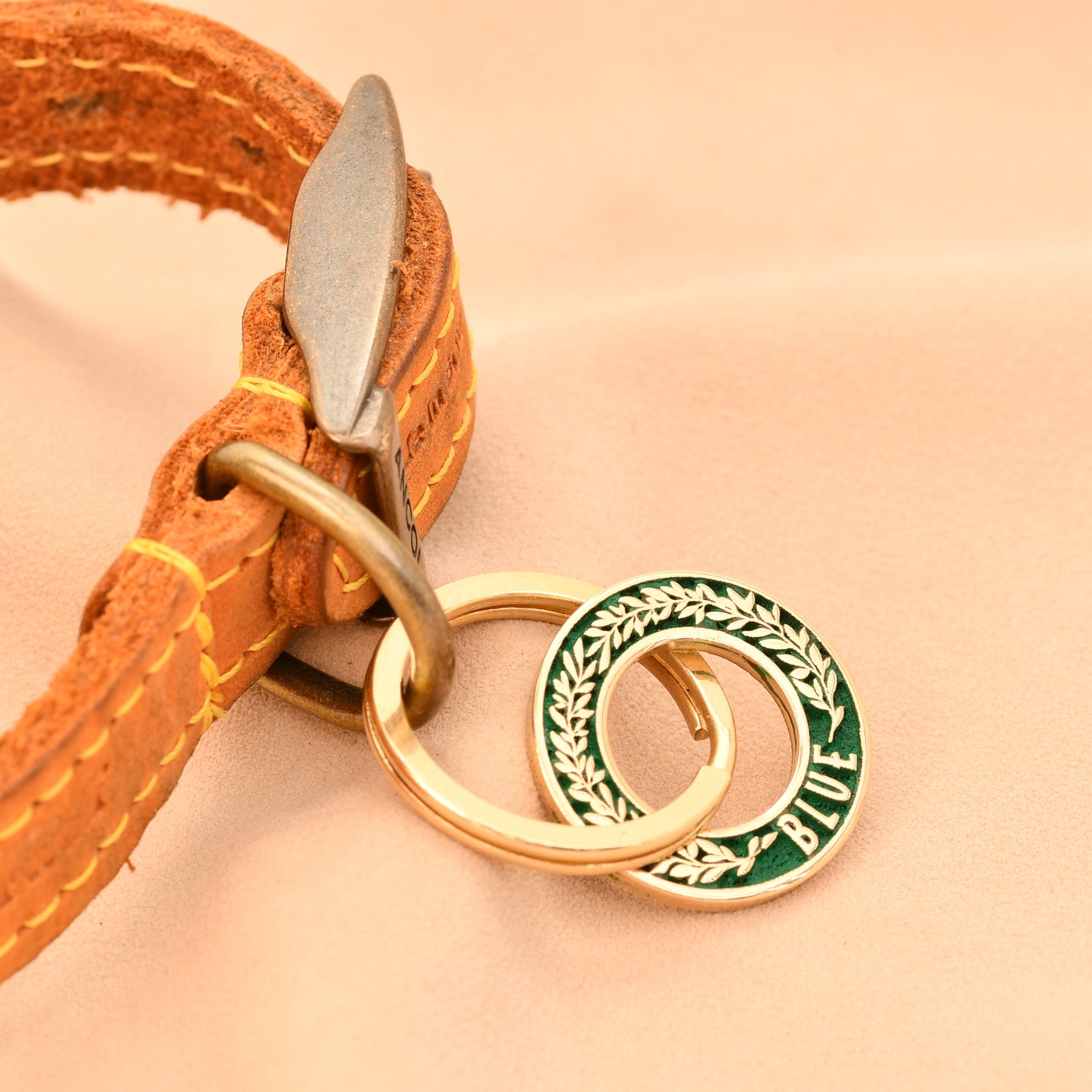 Close-up of a leather strap with a gold and green circular charm on a beige background