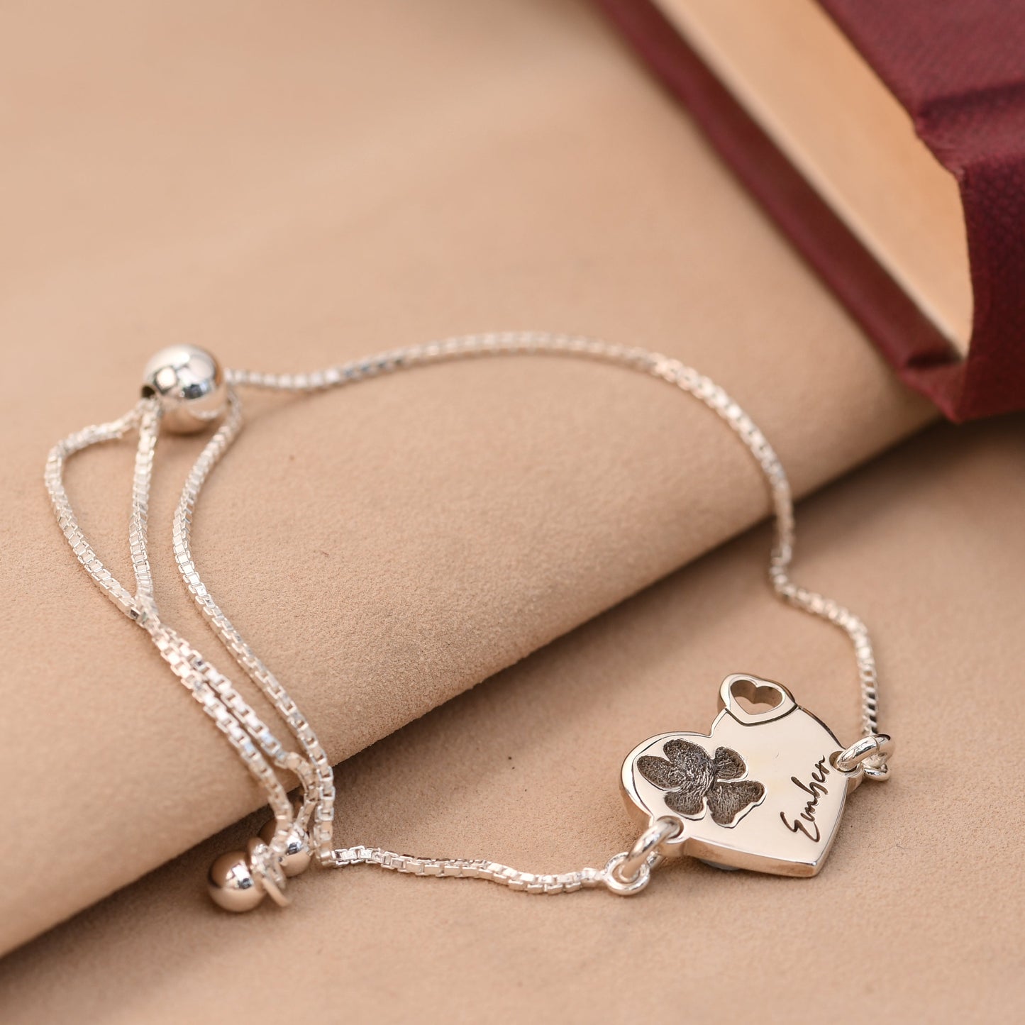 Silver bracelet with heart-shaped charm and engraved text on a beige surface