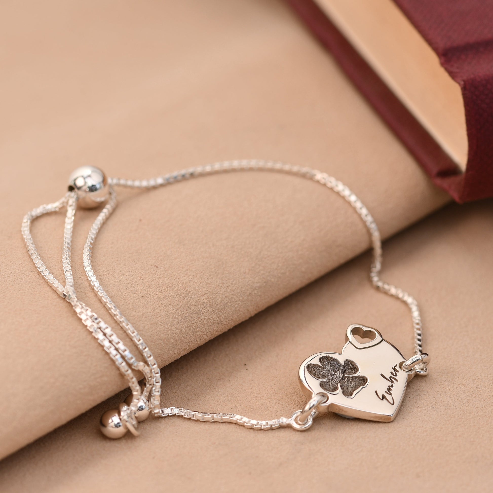 Silver bracelet with heart-shaped charm and engraved text on a beige surface
