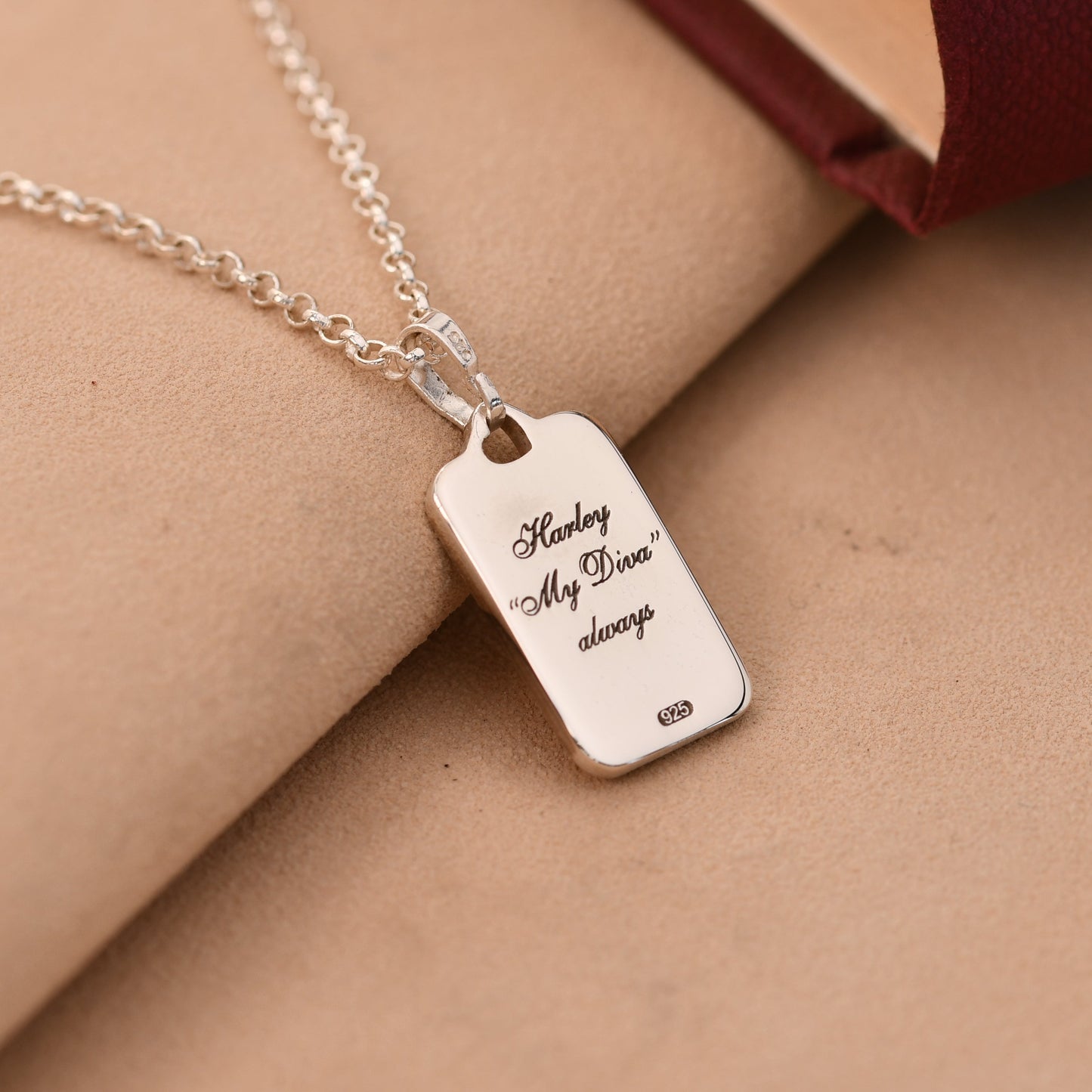 Silver necklace with a engraved tag on a beige surface
