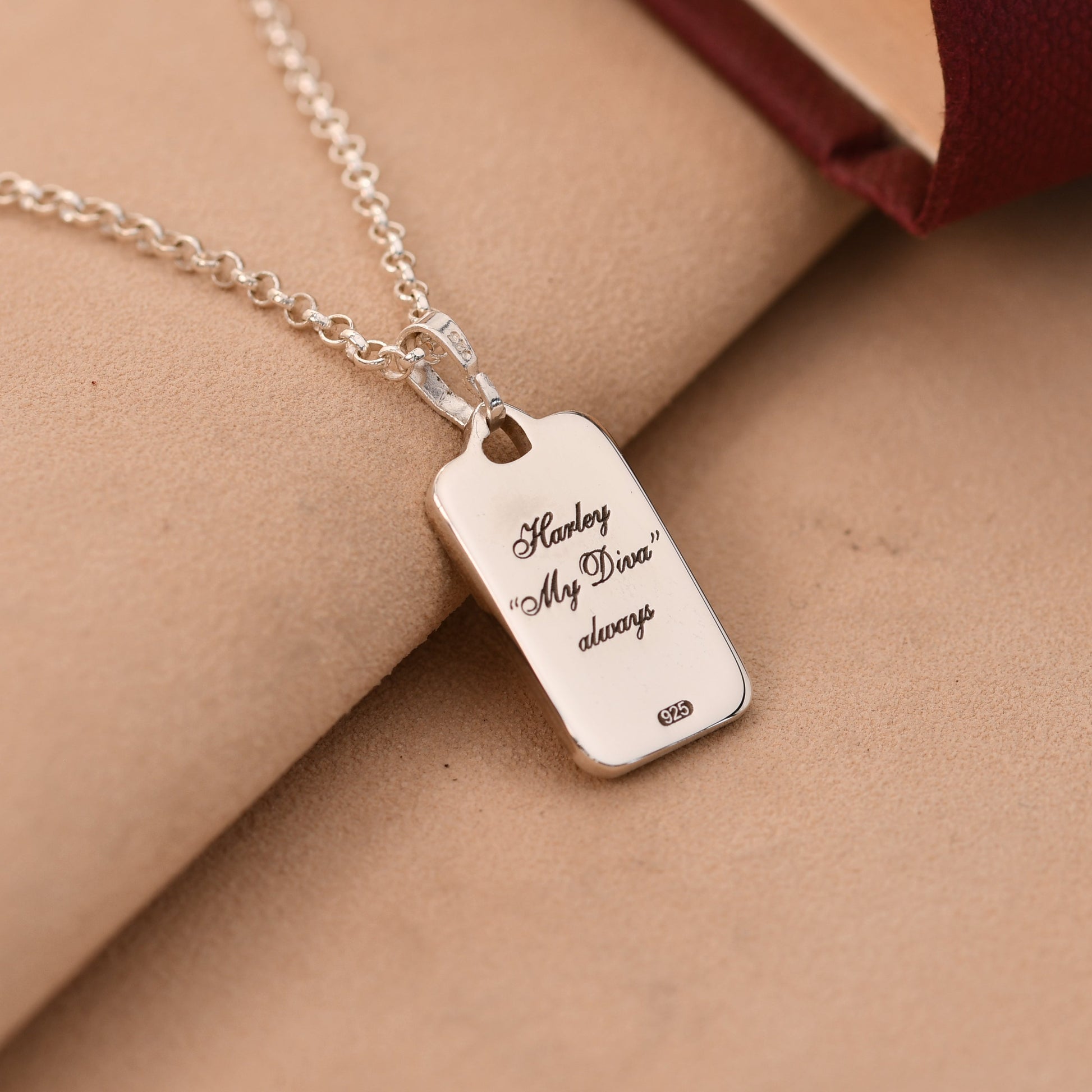 Silver necklace with a engraved tag on a beige surface