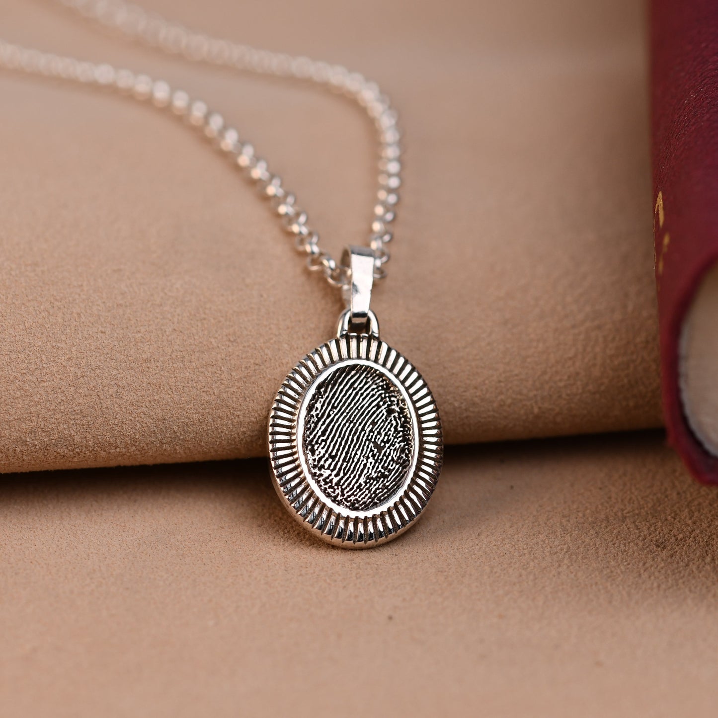 Silver necklace with a round pendant on a beige surface with a red book.