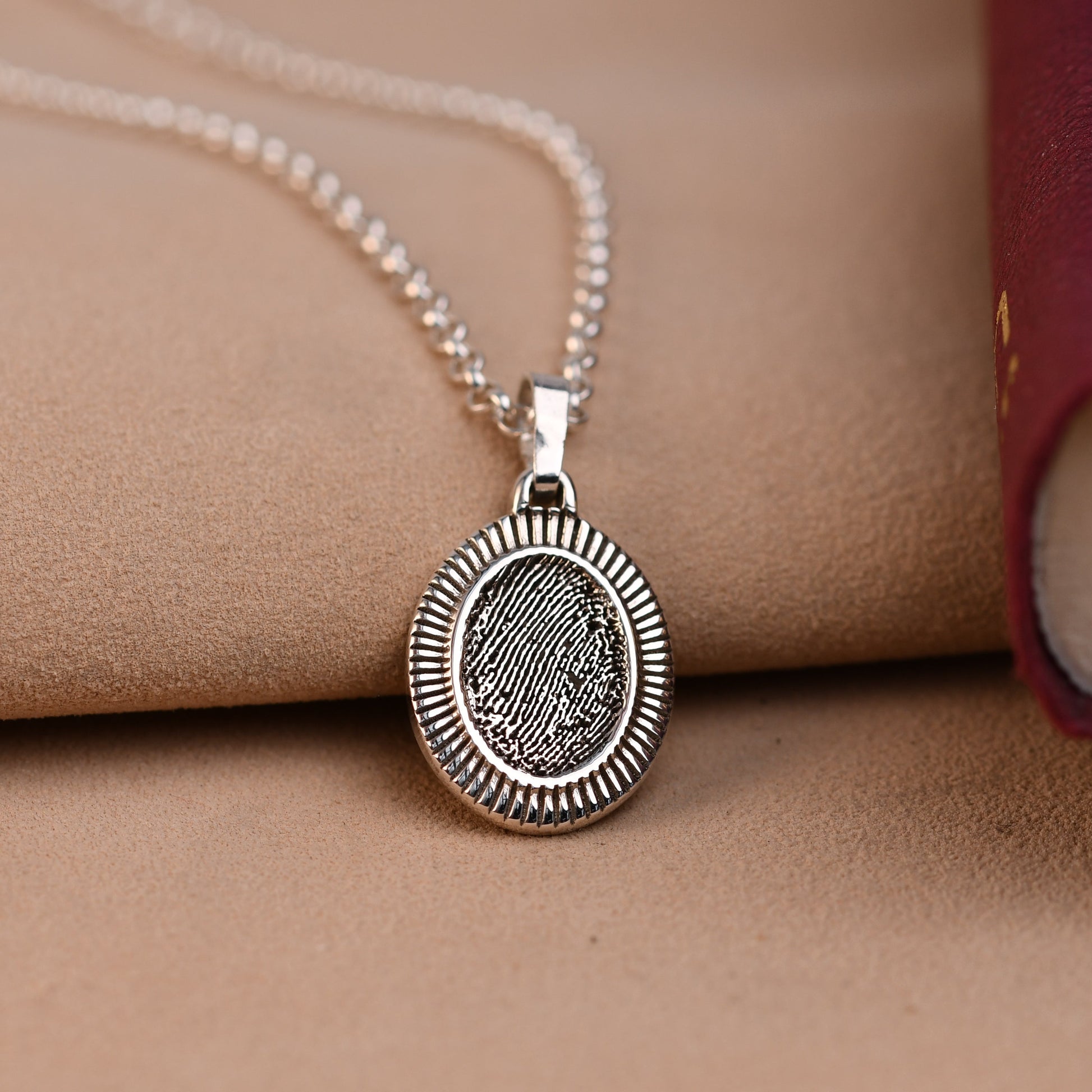 Silver necklace with a round pendant on a beige surface with a red book.