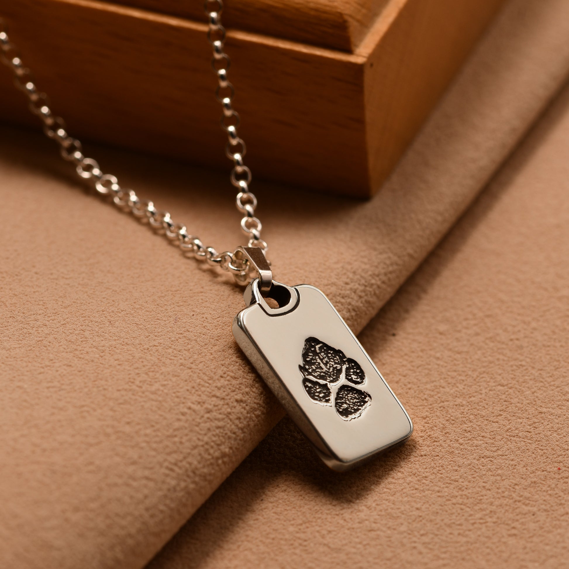 Silver necklace with a dog tag featuring paw prints on a brown surface