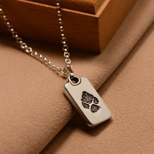Silver necklace with a dog tag featuring paw prints on a brown surface