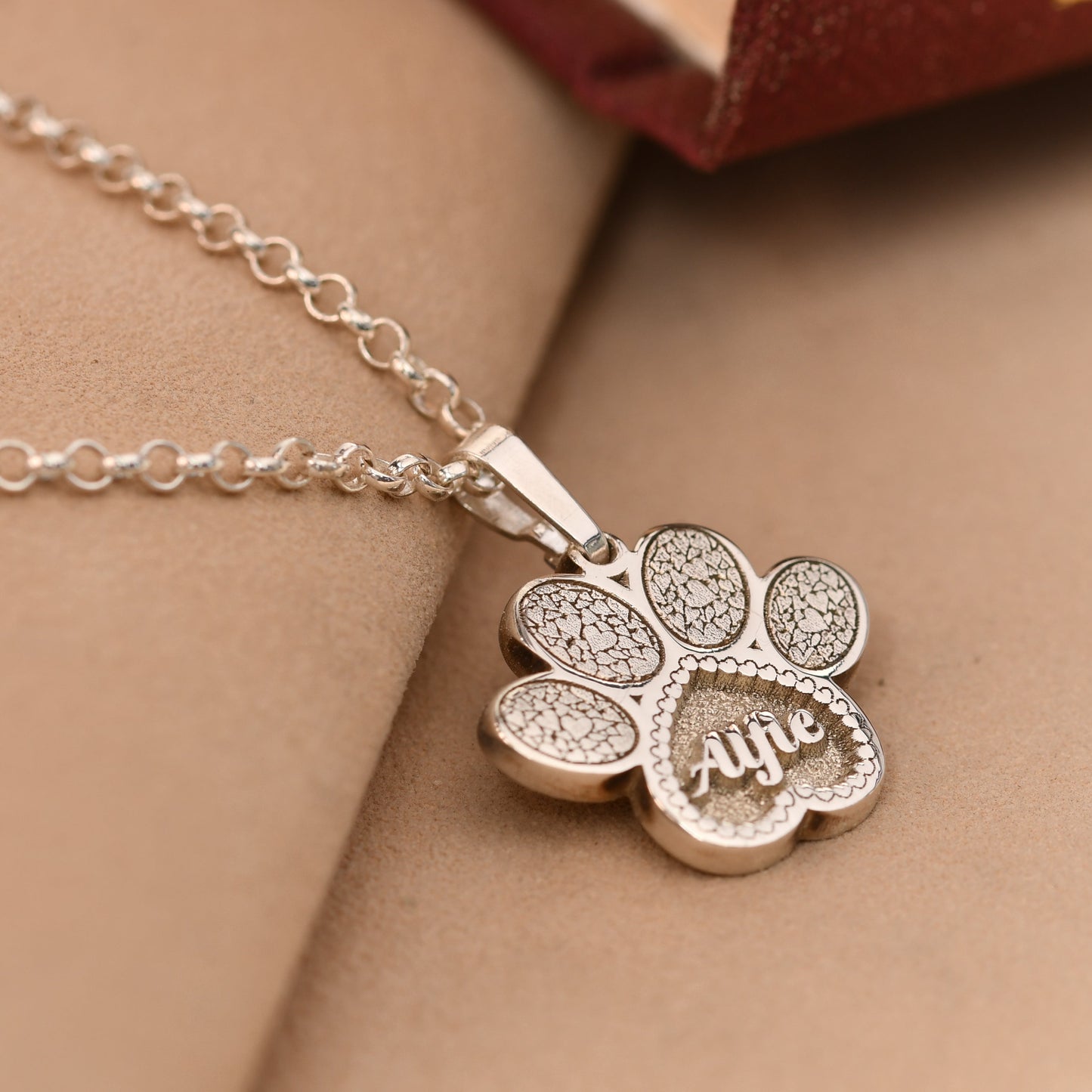 Silver necklace with a paw-shaped pendant on a beige surface