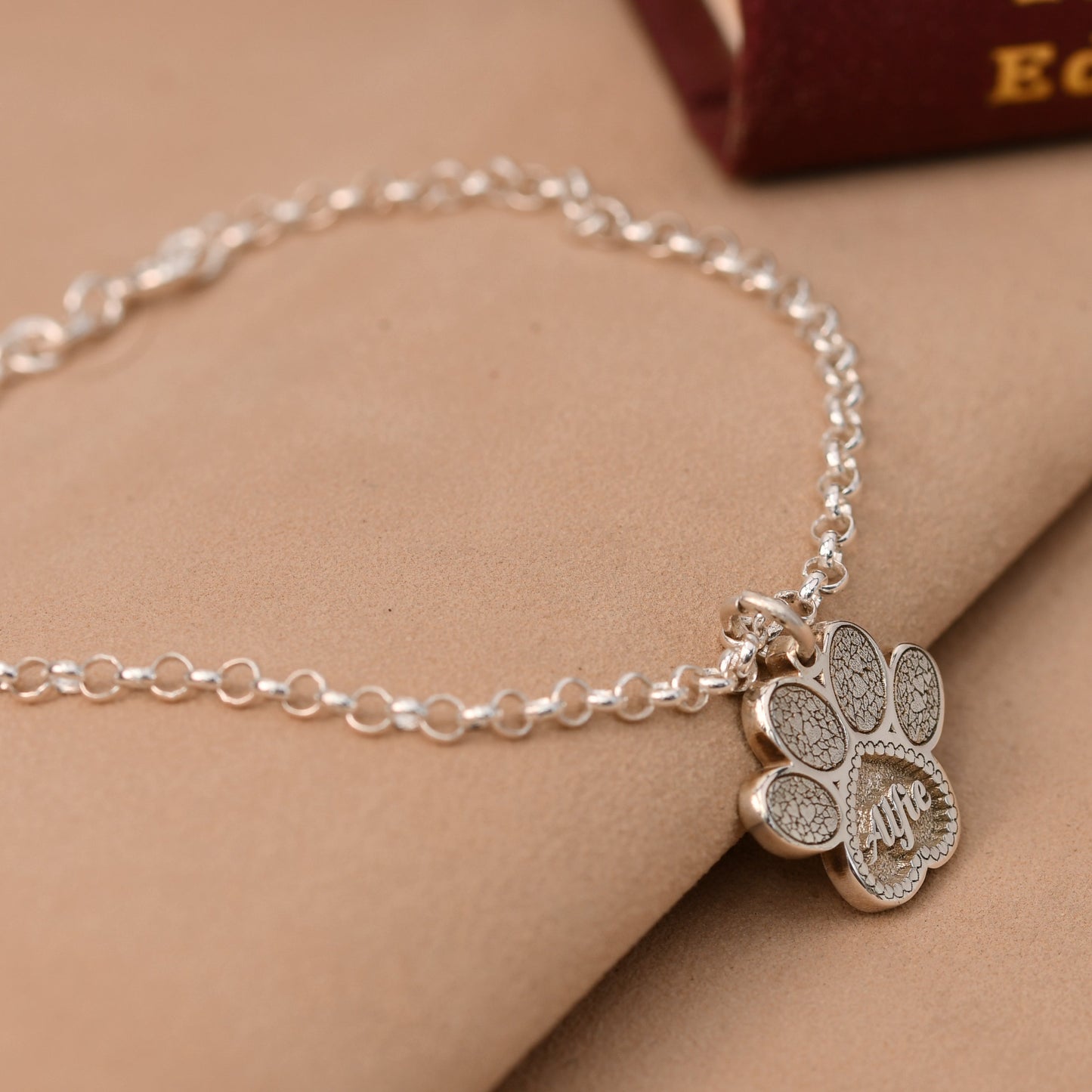 Silver bracelet with a paw-shaped charm on a beige surface