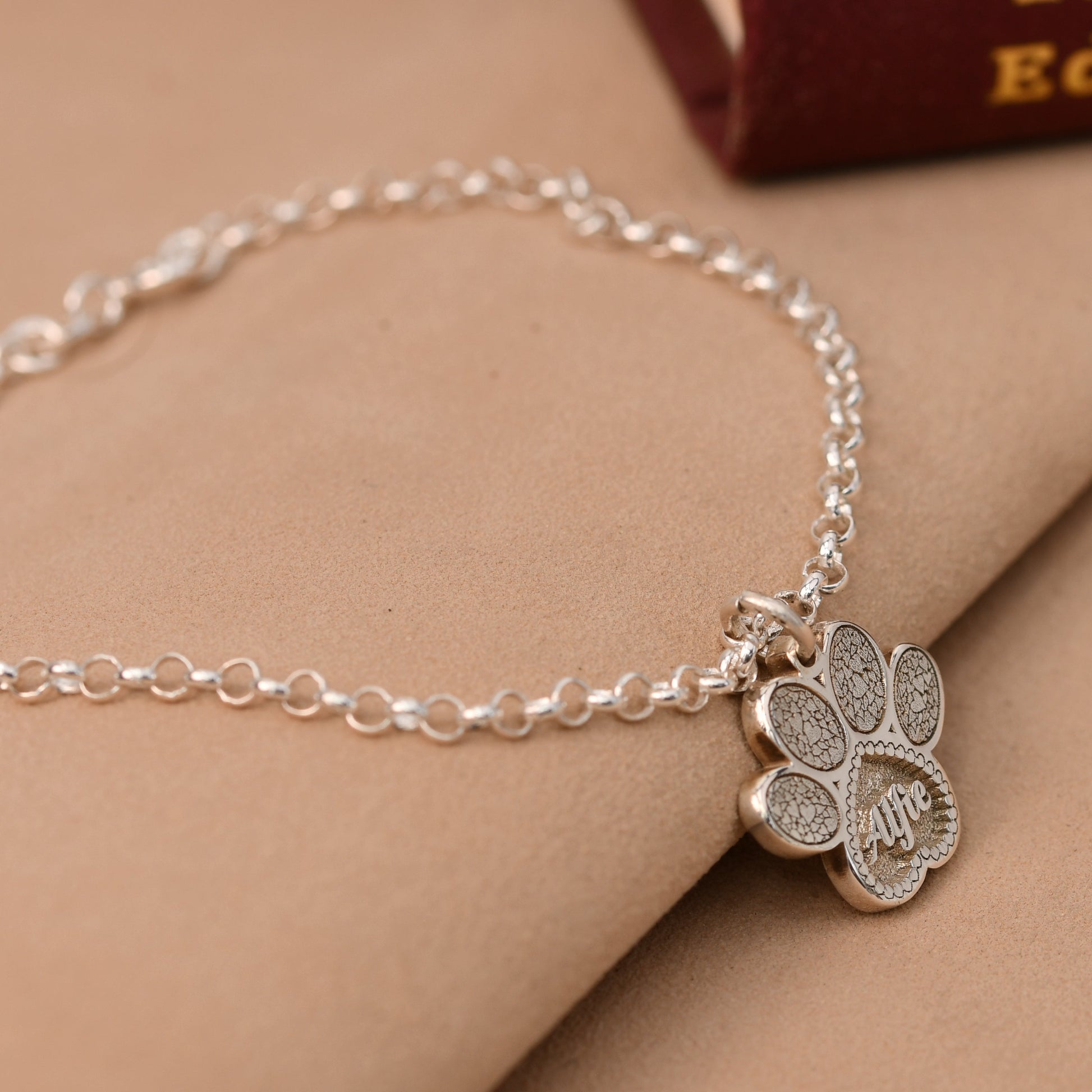 Silver bracelet with a paw-shaped charm on a beige surface