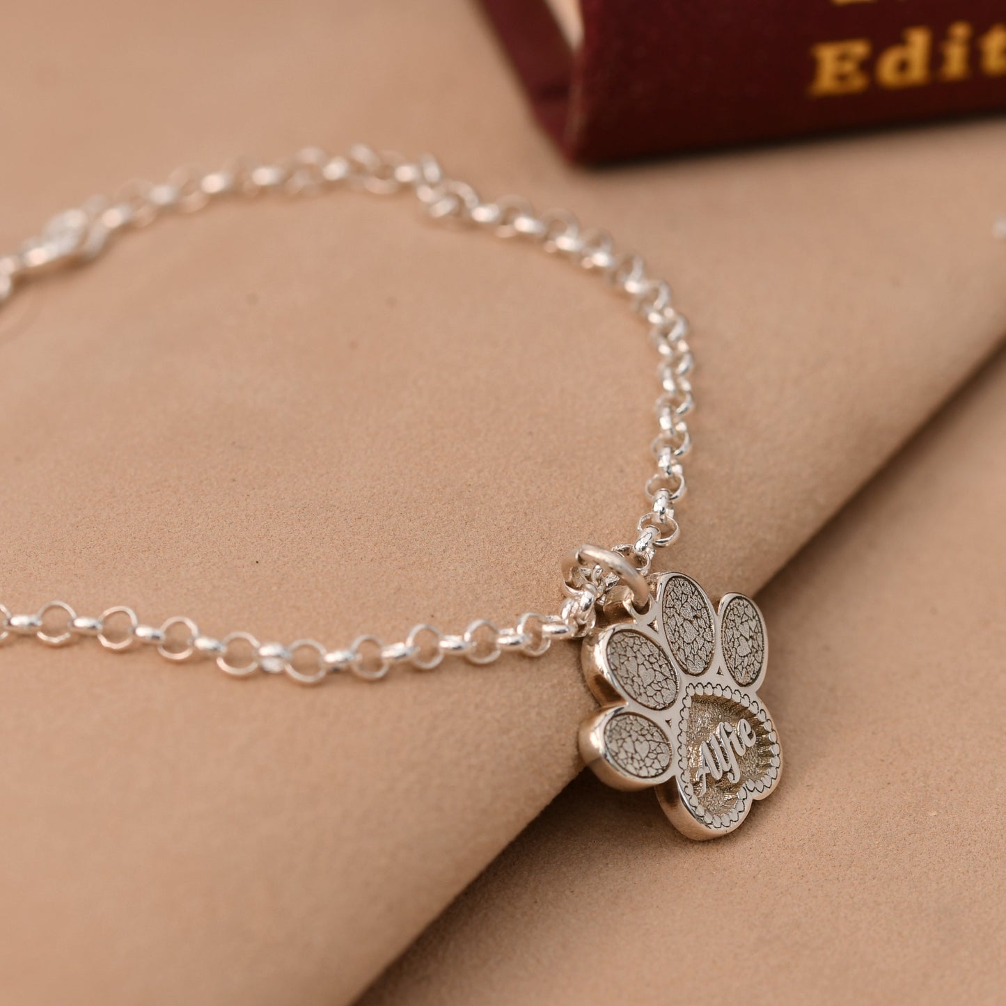 Silver bracelet with a paw-shaped charm on a beige surface