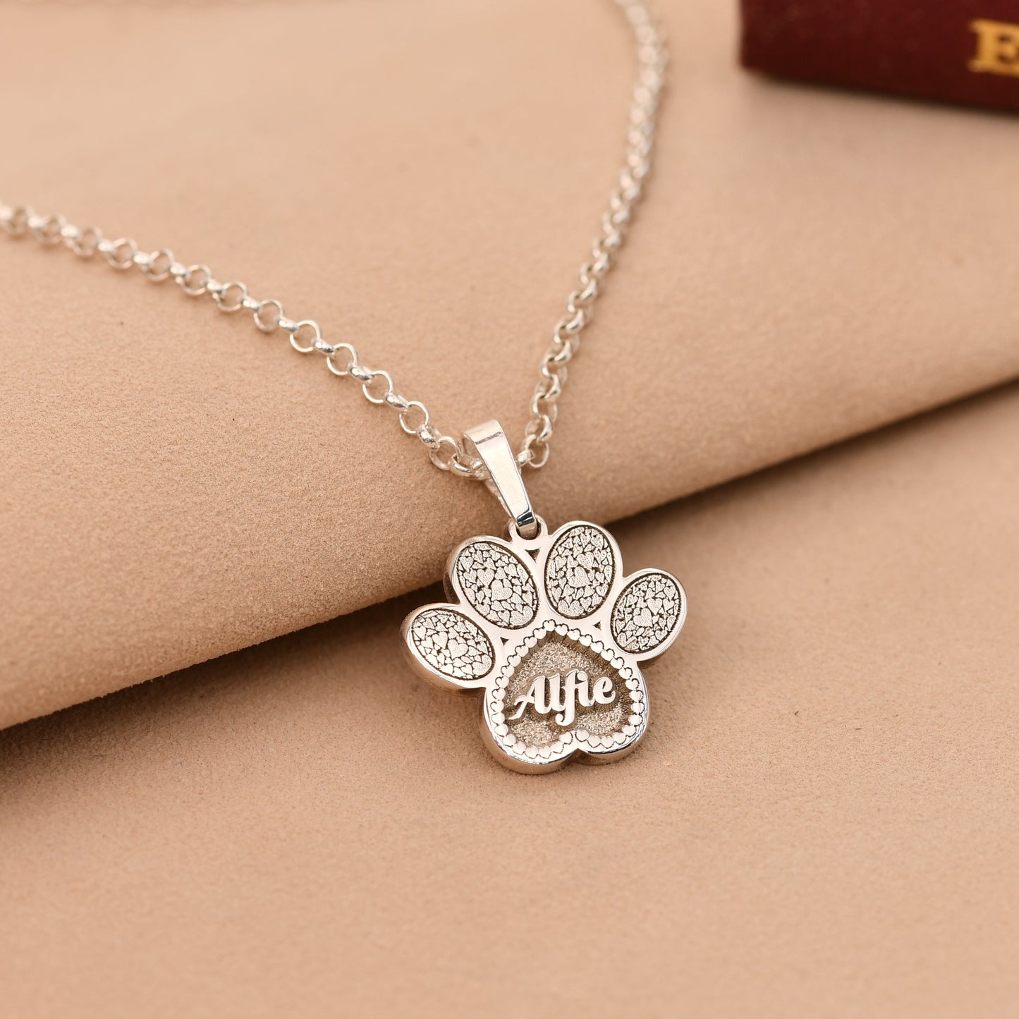 Silver paw print necklace with 'Alife' engraving on a beige surface