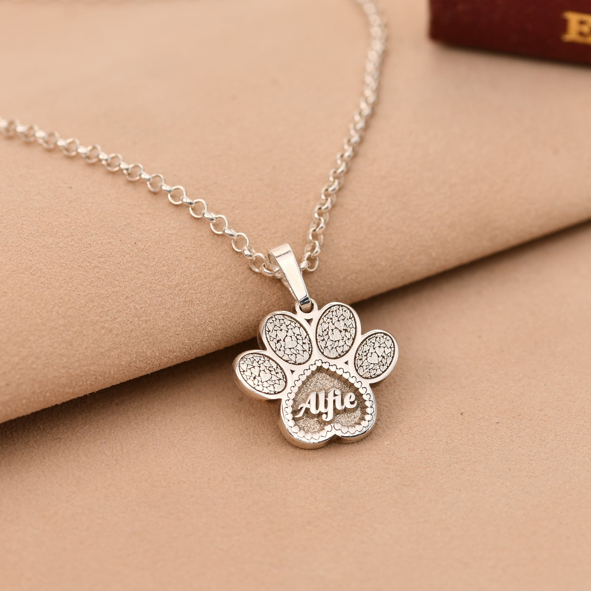 Silver paw print necklace with 'Alife' engraving on a beige surface