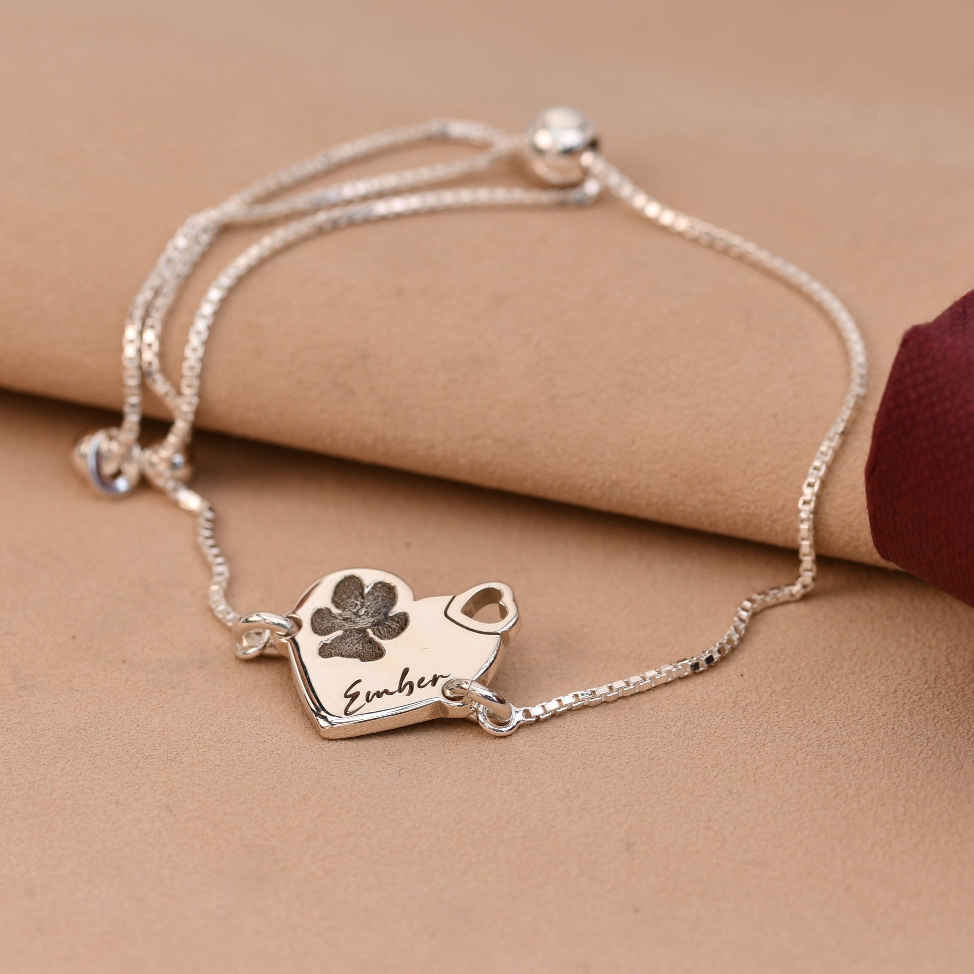 Silver bracelet with paw print charm on a beige surface