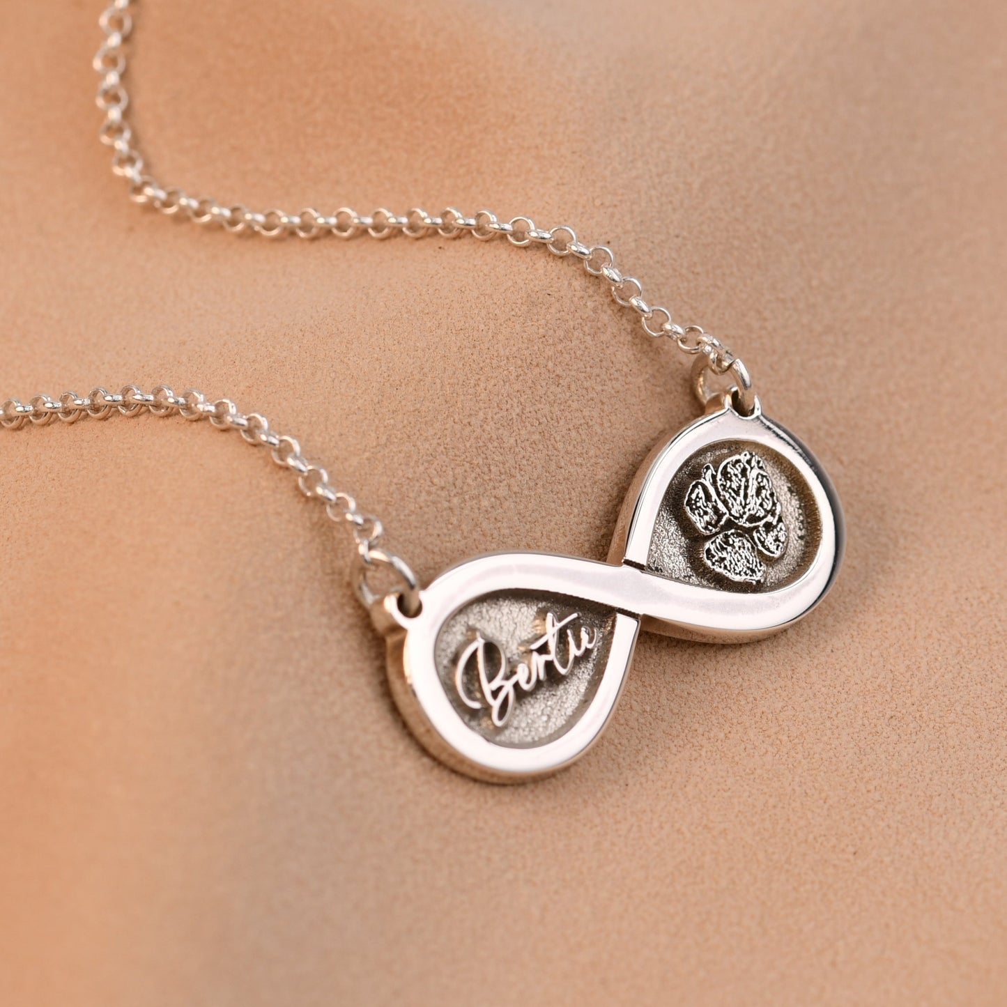 Silver infinity necklace with paw prints on a beige background