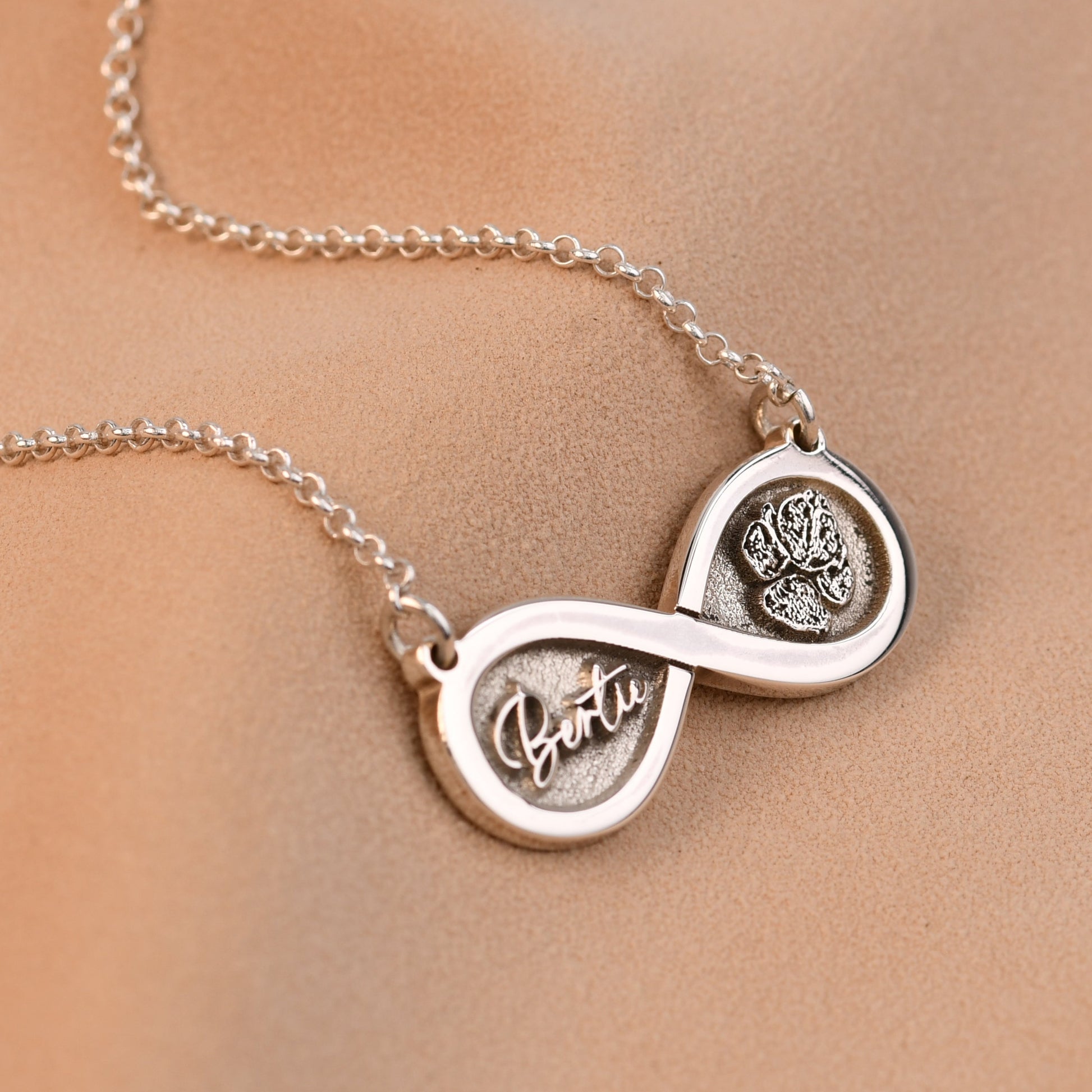 Silver infinity necklace with paw prints on a beige background