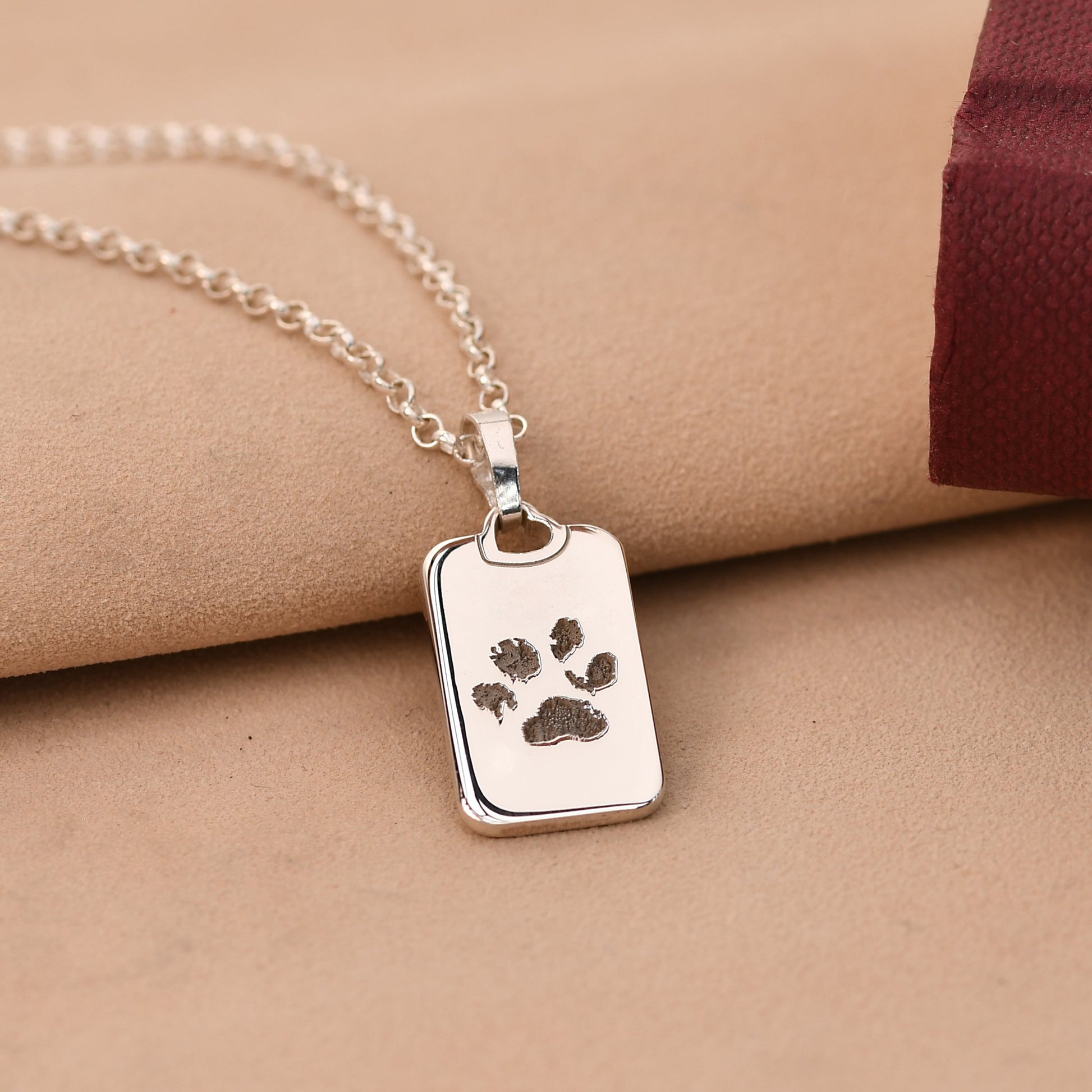Silver necklace with a paw print pendant on a beige surface with a book in the background.